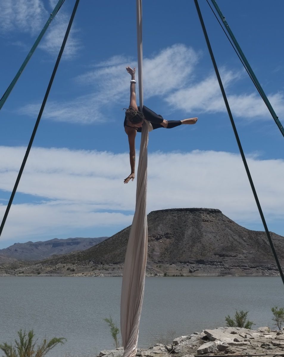 Woman doing aerial silks in front of a dramatic desert landscape