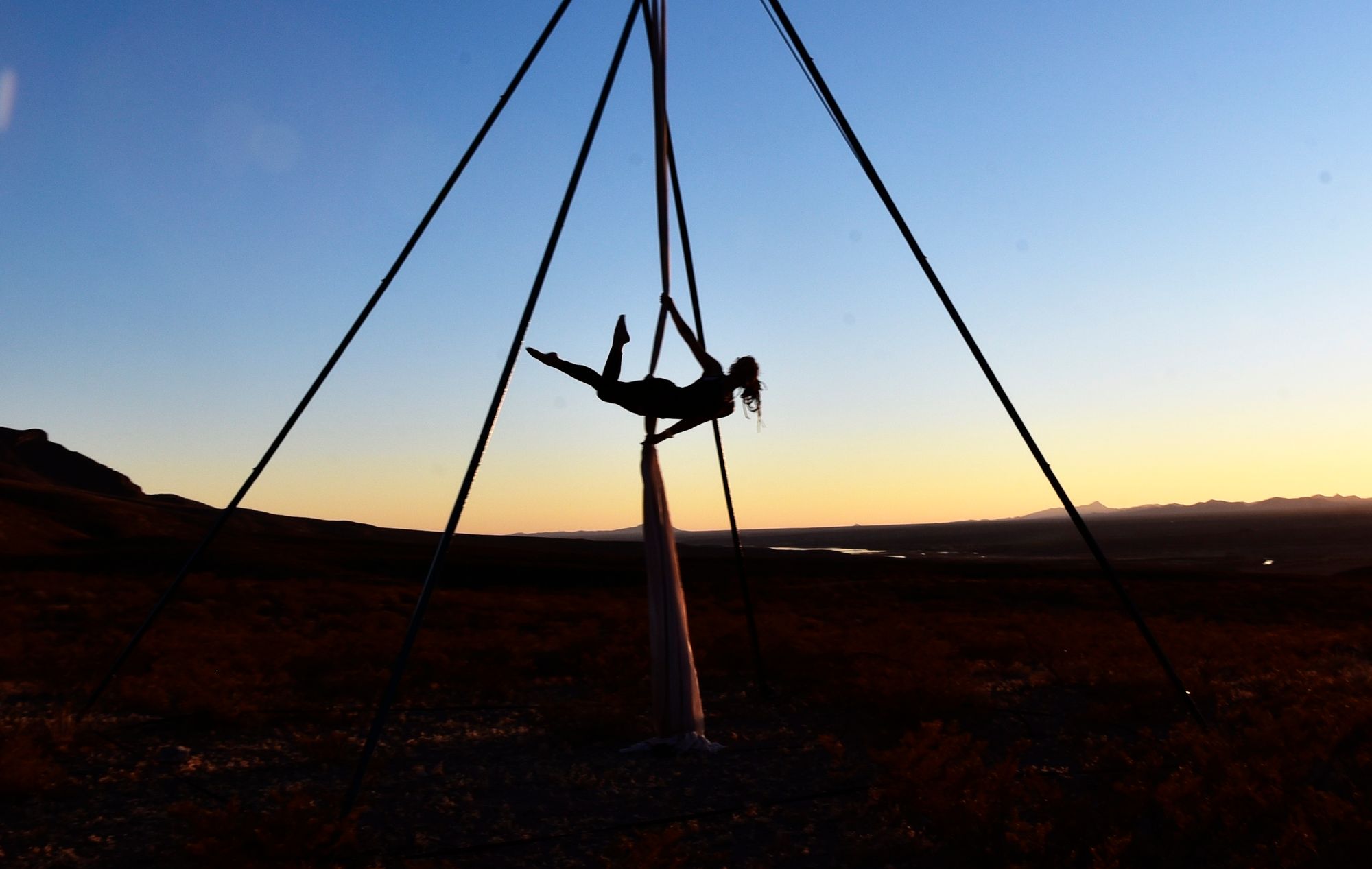 Woman silhouetted at sunset doing aerial acrobatics in the mountains 