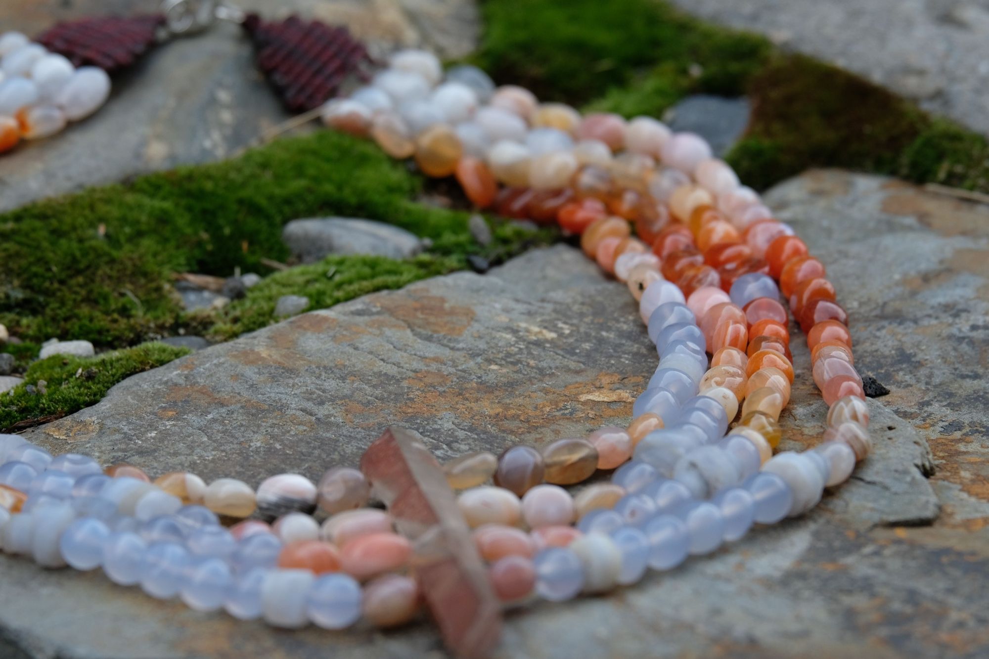 Detail of clear quartz point, red-pink-white graded Botswana agate and blue chalcedony necklace laying on stone