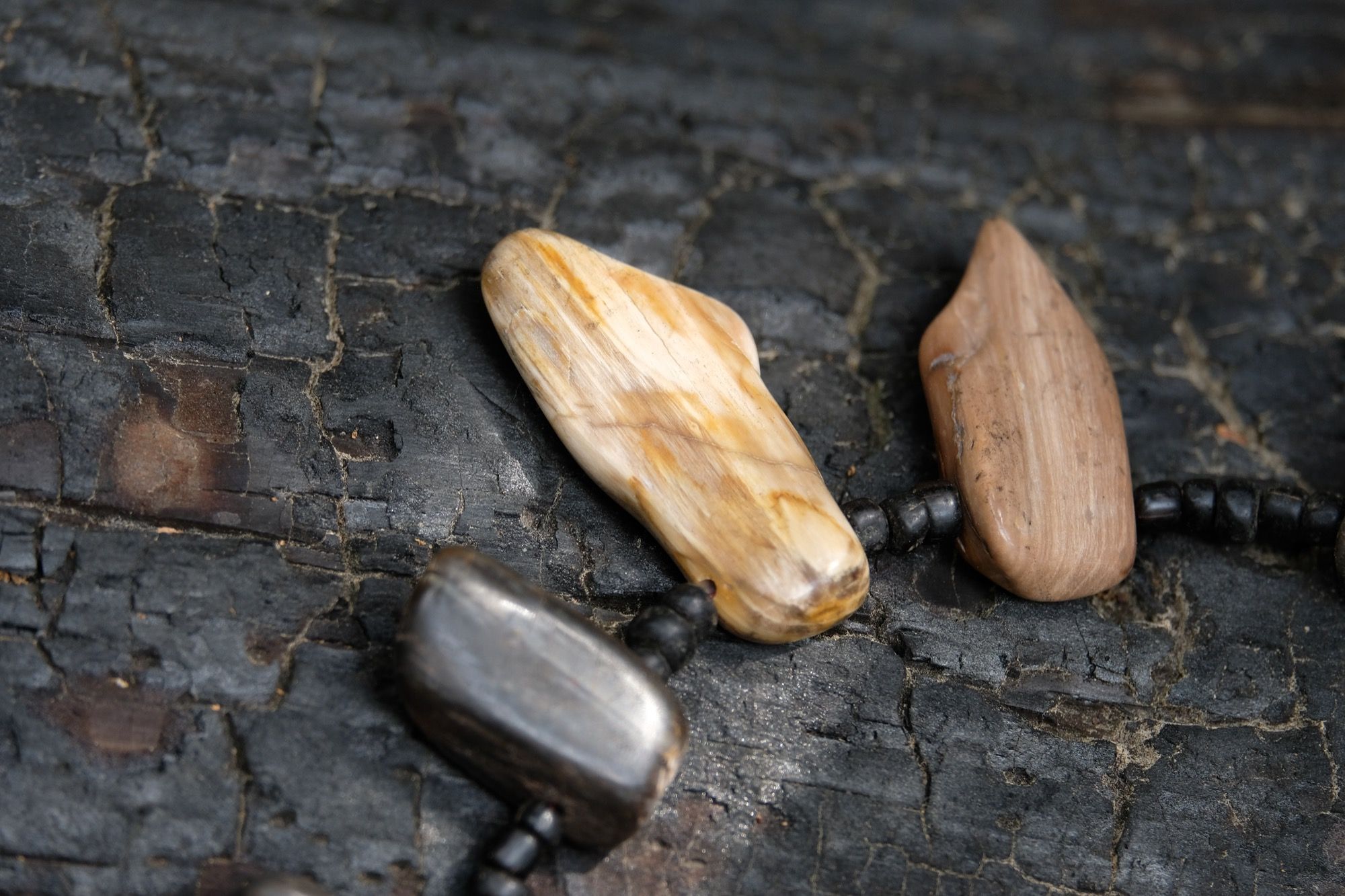 Detail of necklace with petrified wood and black beads sitting on a burned log