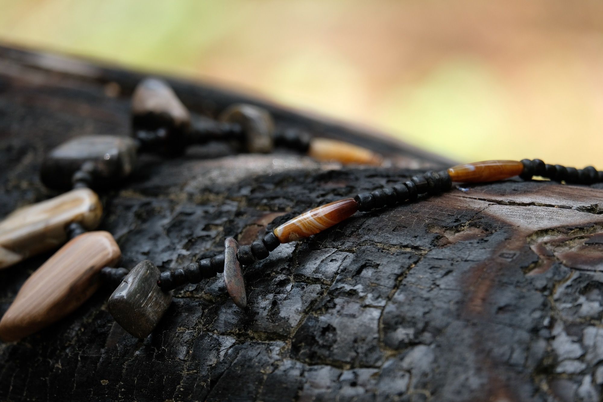 Detail of necklace with petrified wood and black beads sitting on a burned log