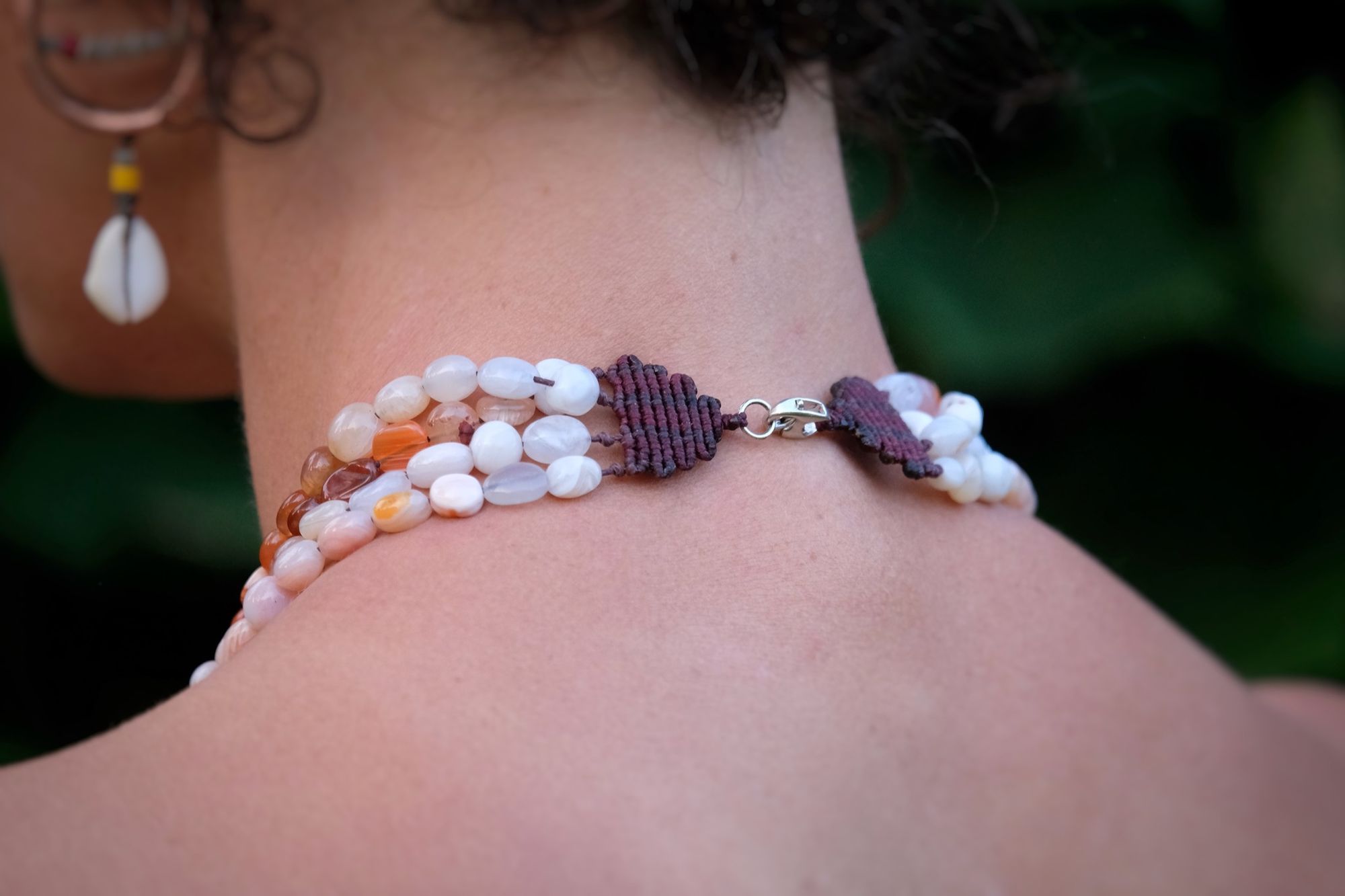 woman wearing clear quartz point, red-pink-white graded Botswana agate and blue chalcedony necklace laying on stone