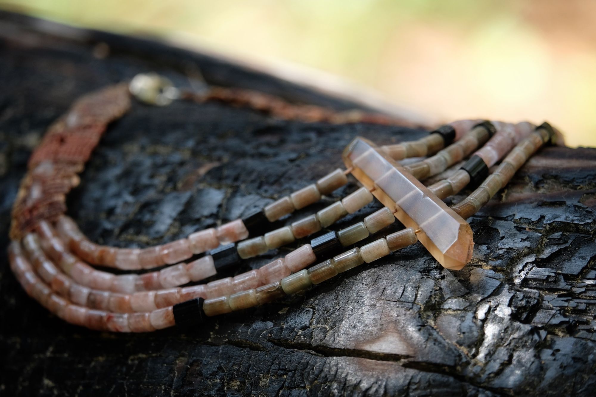 Four strand Zambian citrine, pink Rutilated quartz and black tourmaline necklace laying on a burned log
