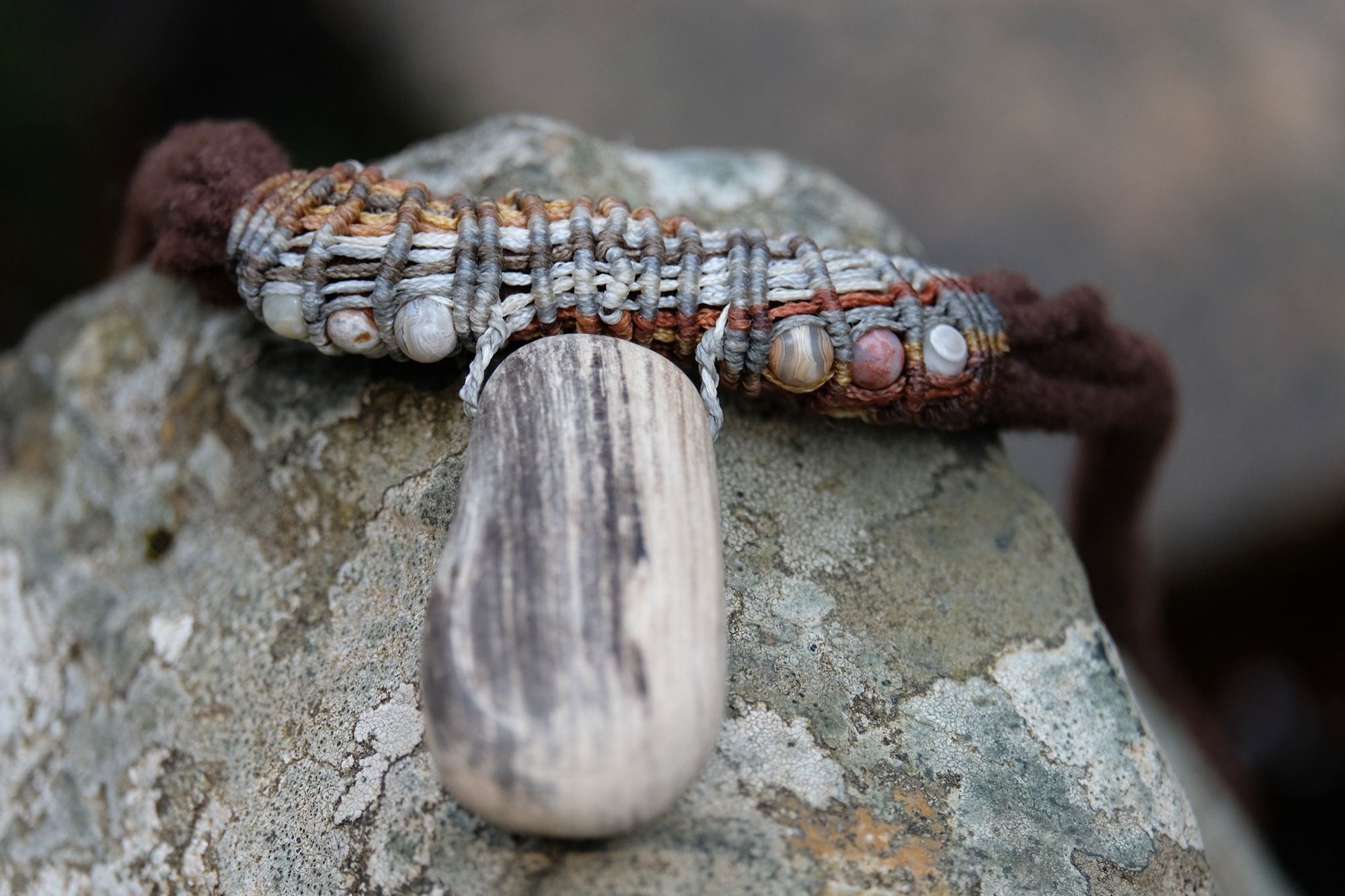 Detail of sculptural necklace made of brown felt, petrified wood and grey-brown knotwork laying on a lichen covered stone