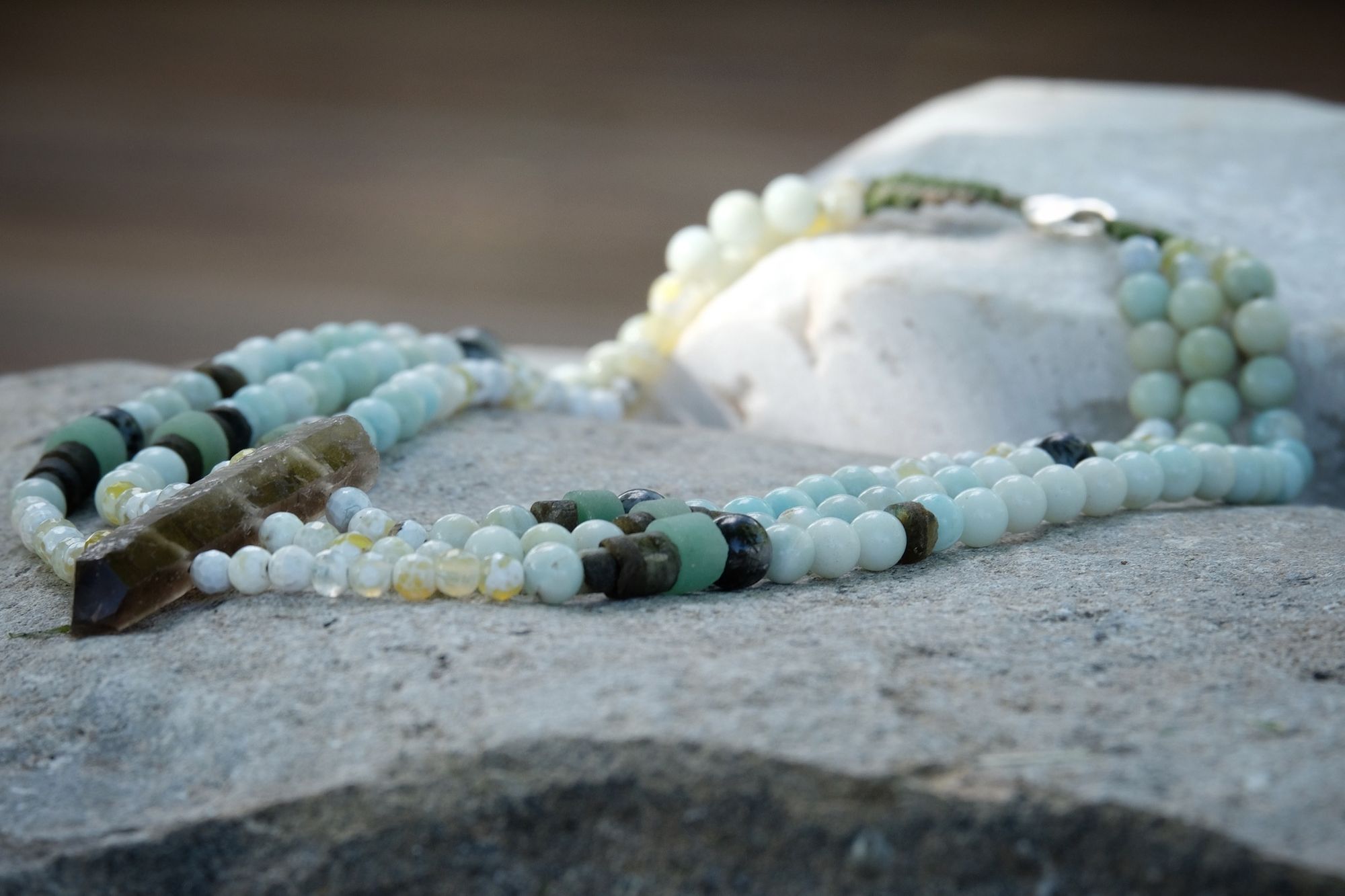 Smoky quartz, fire agate, Amazonite, labradorite, aventurine and rutilated quartz necklace laying on a stone