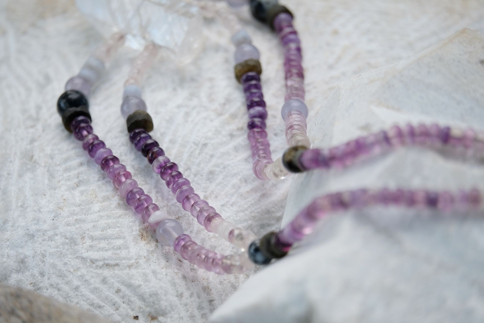 Detail of quartz point, rose quartz, blue chalcedony, purple fluorite and labradorite necklace laying on a rock