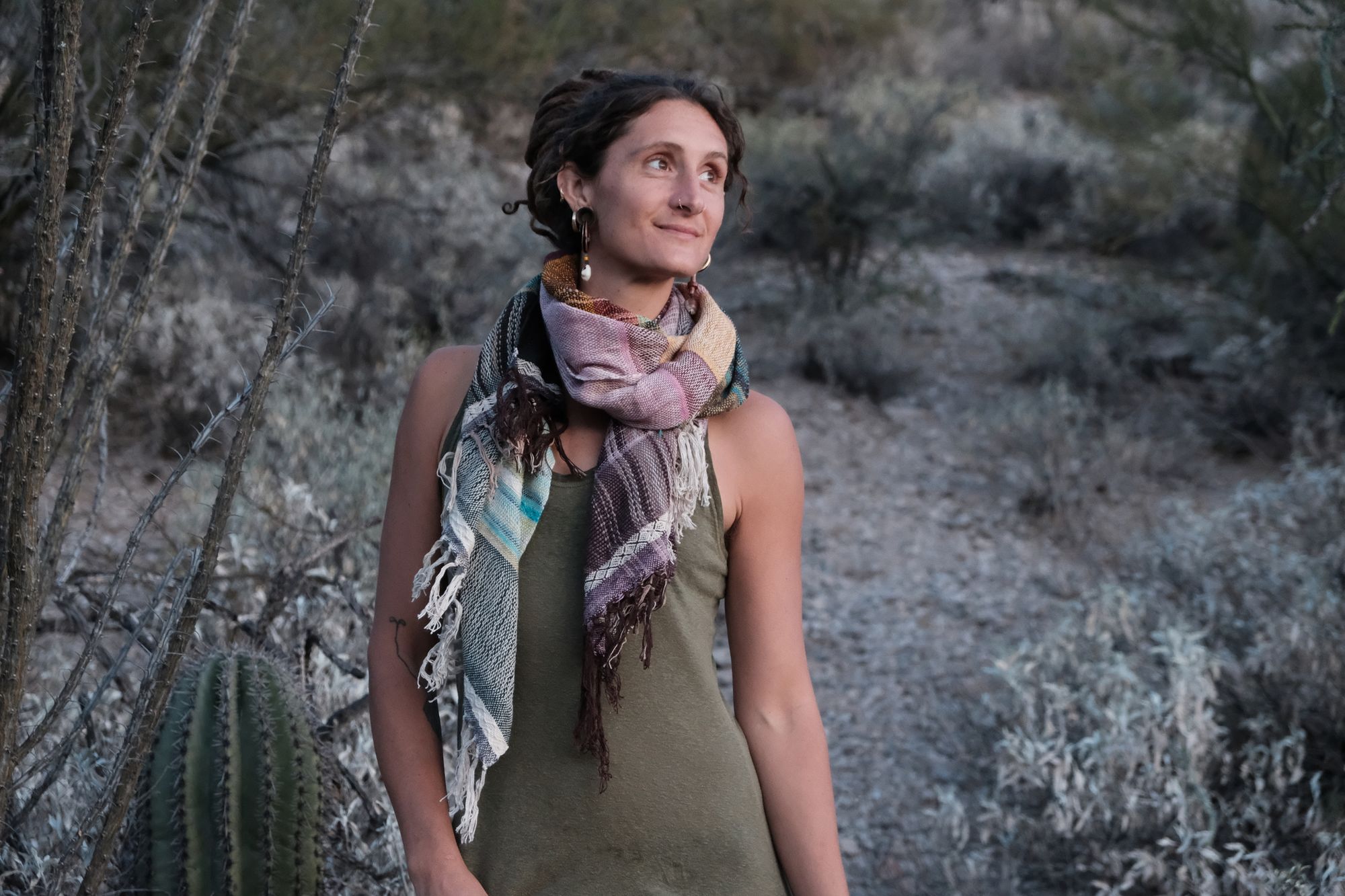 Woman wearing a blue, purple, white, brown and green scarf in the desert. 