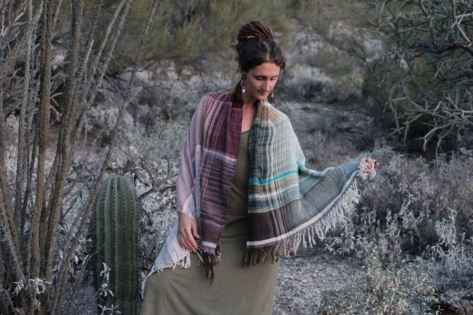 Woman wearing a blue, purple, white, brown and green scarf in the desert. 