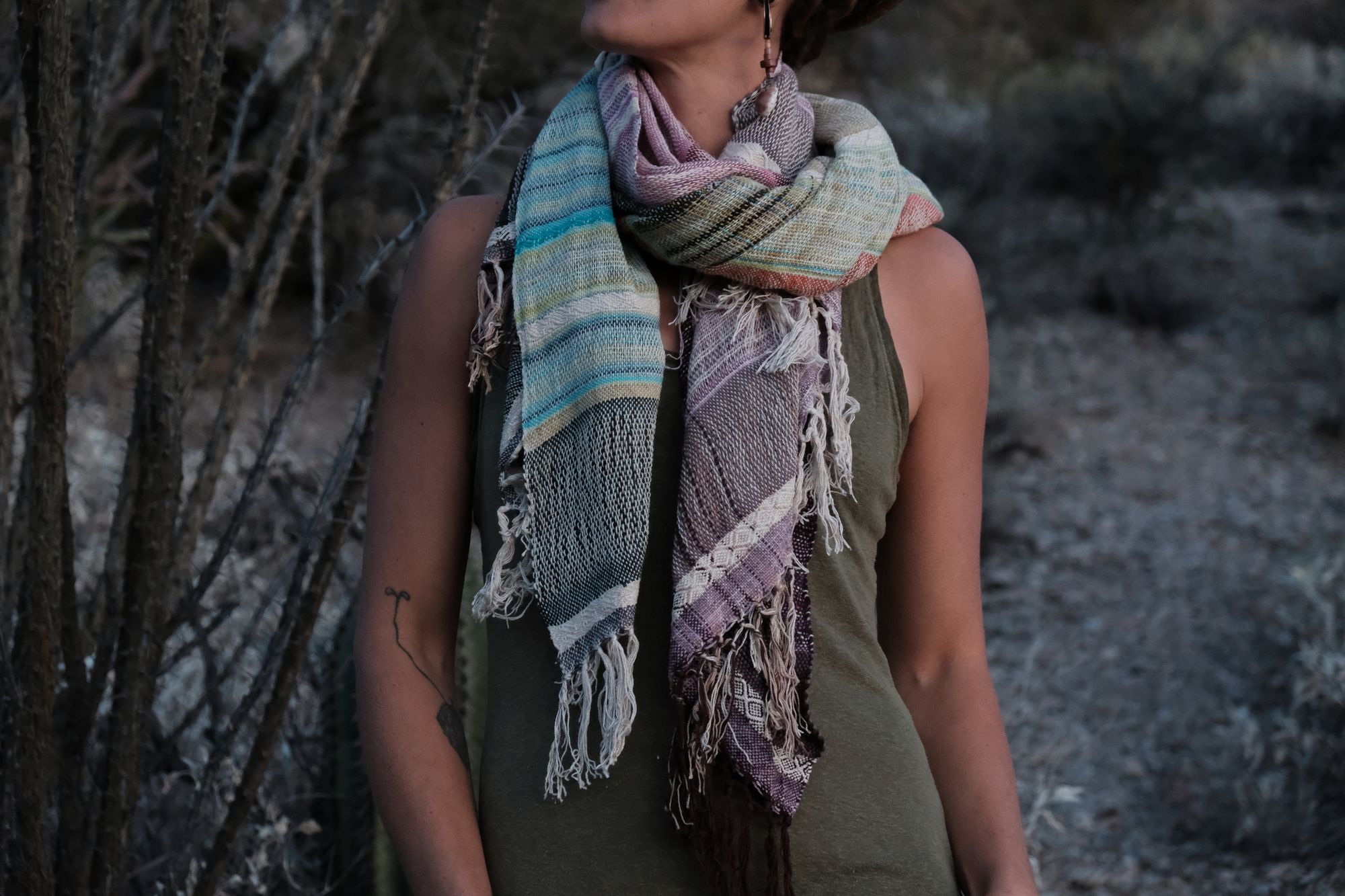 Woman wearing a blue, purple, white, brown and green scarf in the desert. 