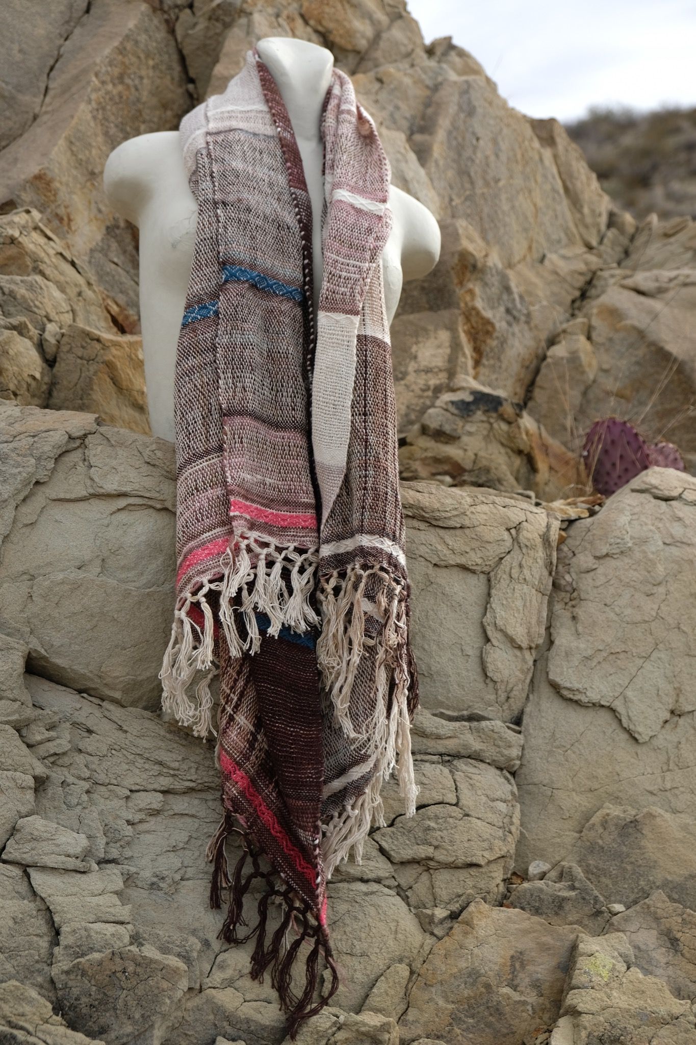 Pink, blue, maroon, white and brown handwoven textured scarf on a white mannequin in the desert 