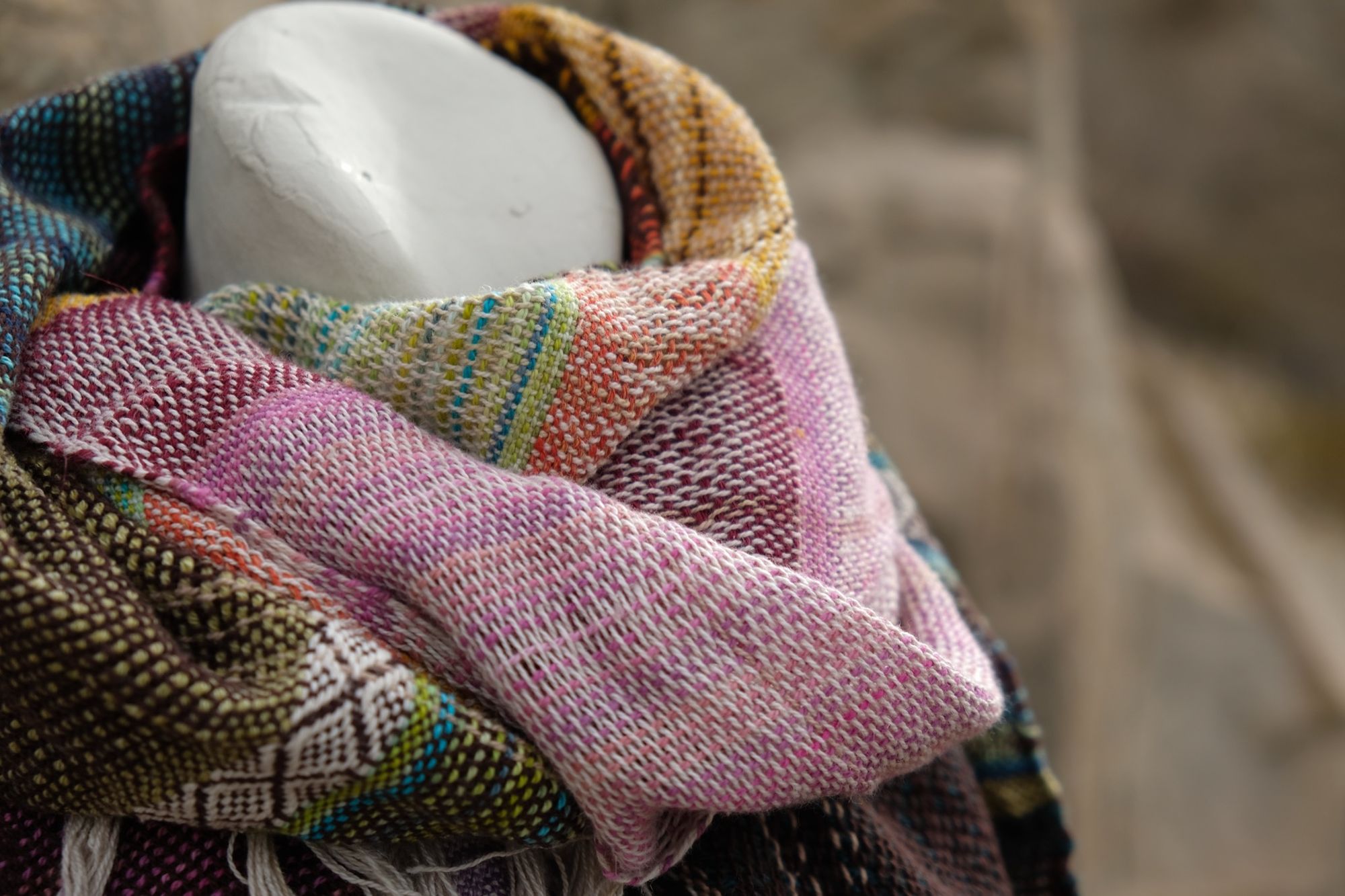 Pink, green, yellow, blue, white, orange and brown handwoven textured scarf on a white mannequin in the desert 