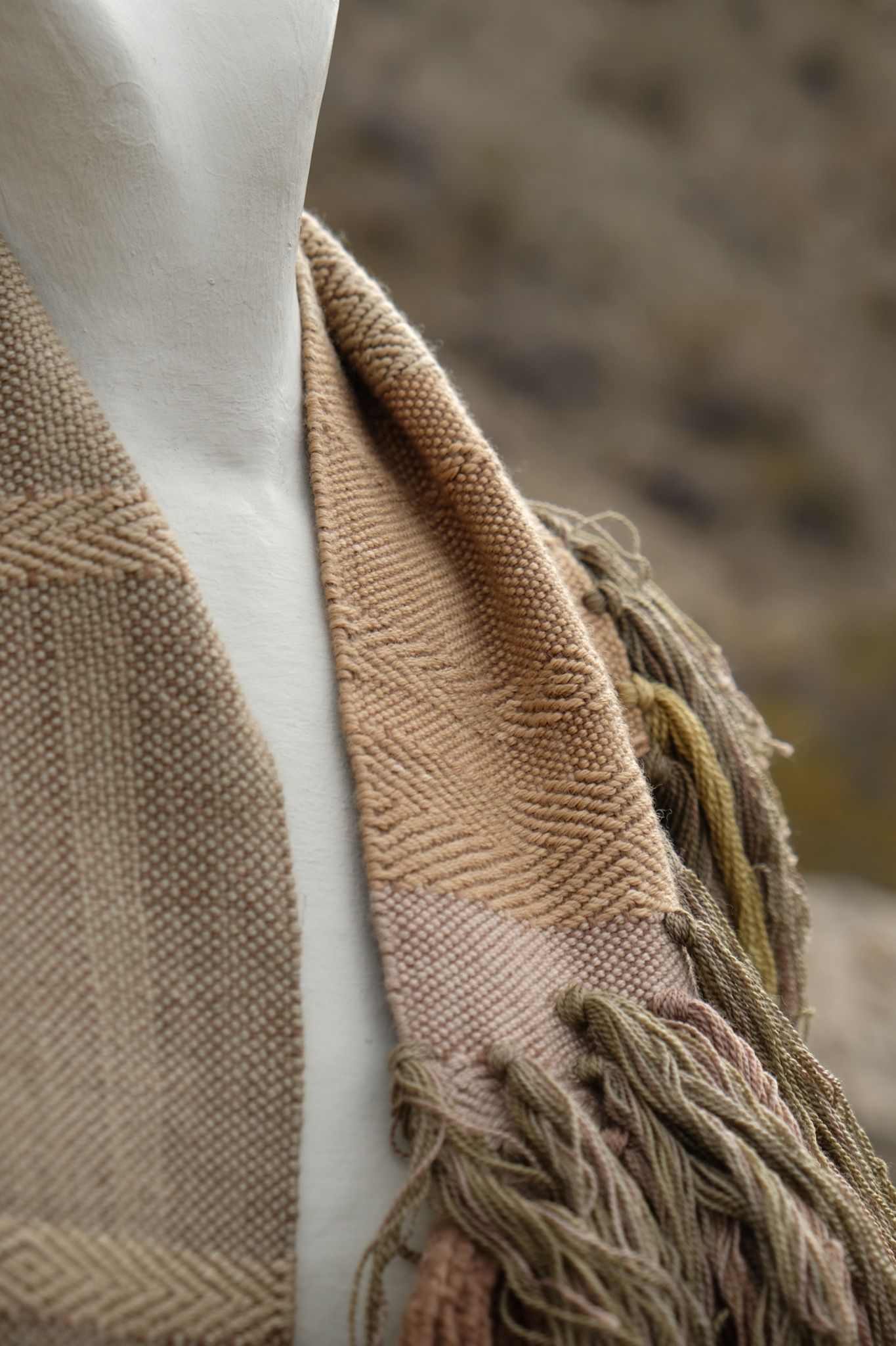 detail of naturally dyed brown, green and tan fringed infinity scarf on a white mannequin bust in the desert