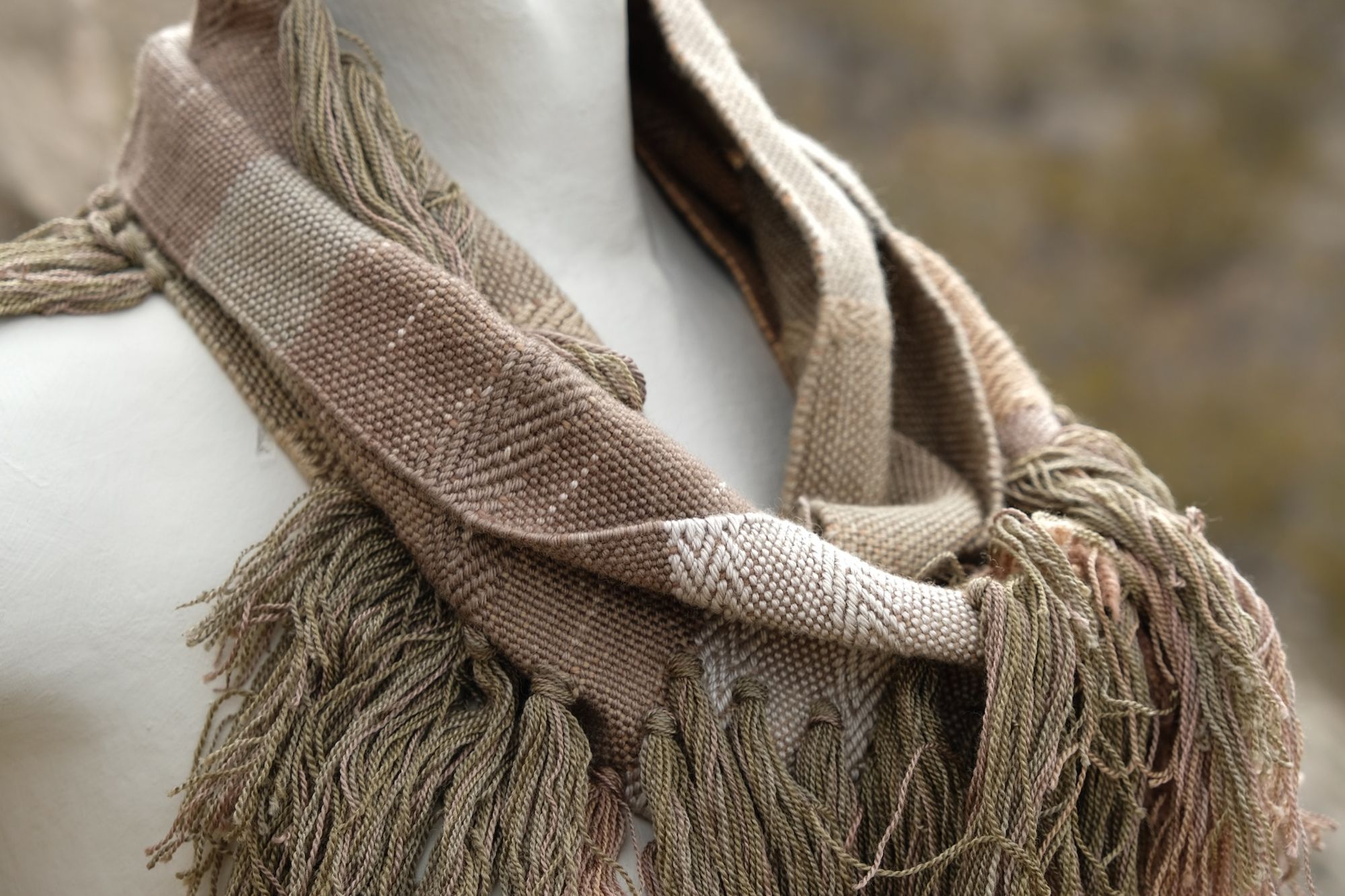 detail of naturally dyed brown, green and tan fringed infinity scarf on a white mannequin bust in the desert