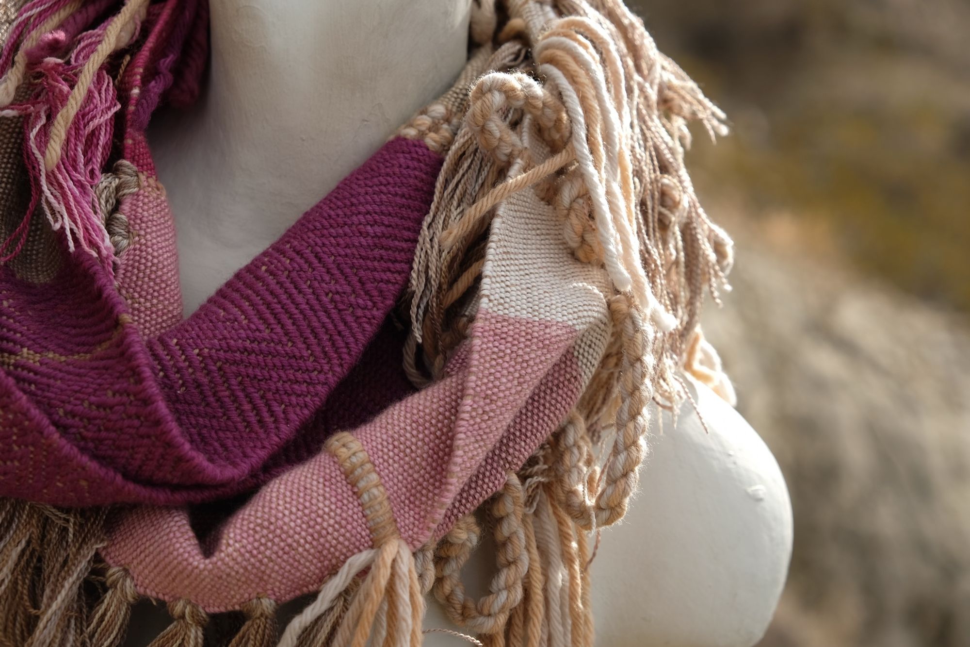 detail of naturally dyed brown, fuchsia and tan fringed infinity scarf on a white mannequin bust in the desert