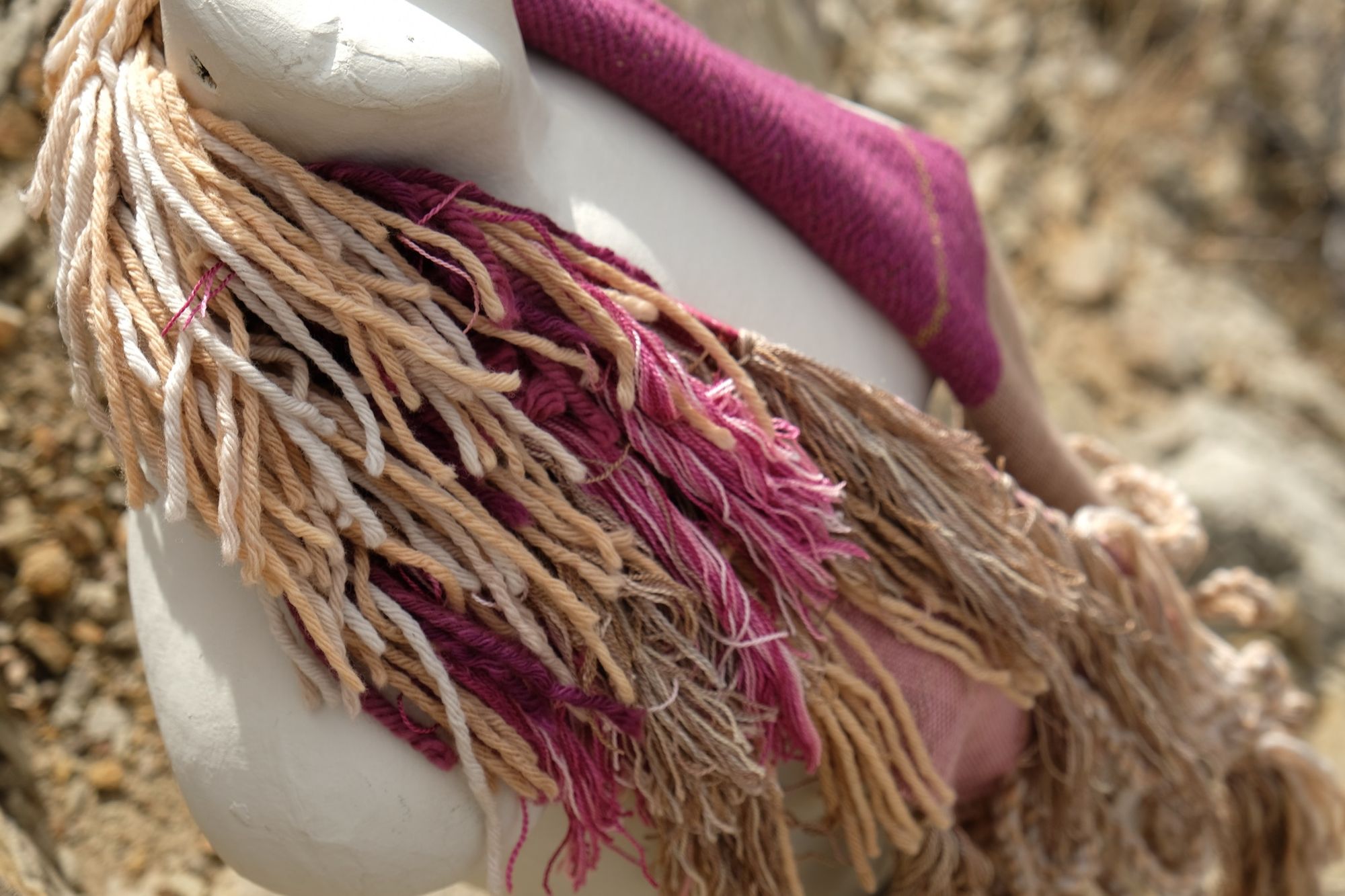 naturally dyed brown, fuchsia and tan fringed infinity scarf on a white mannequin bust in the desert