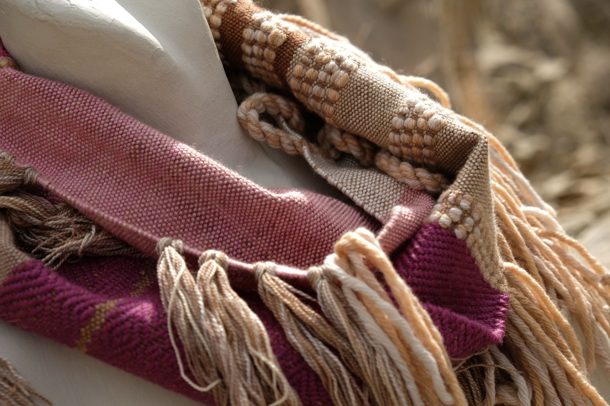 detail of naturally dyed brown, fuchsia and tan fringed infinity scarf on a white mannequin bust in the desert