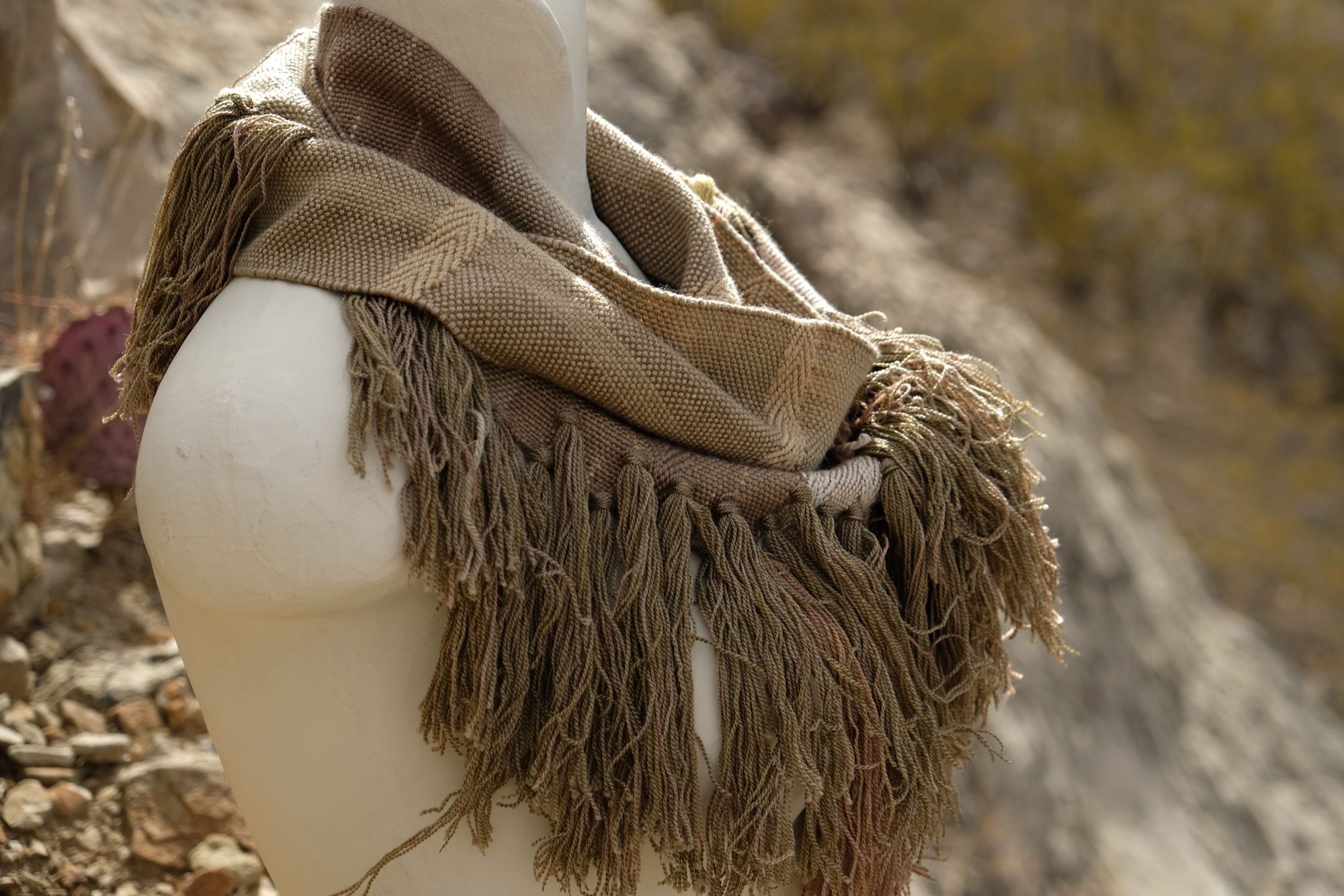 naturally dyed brown, green and tan fringed infinity scarf on a white mannequin bust in the desert