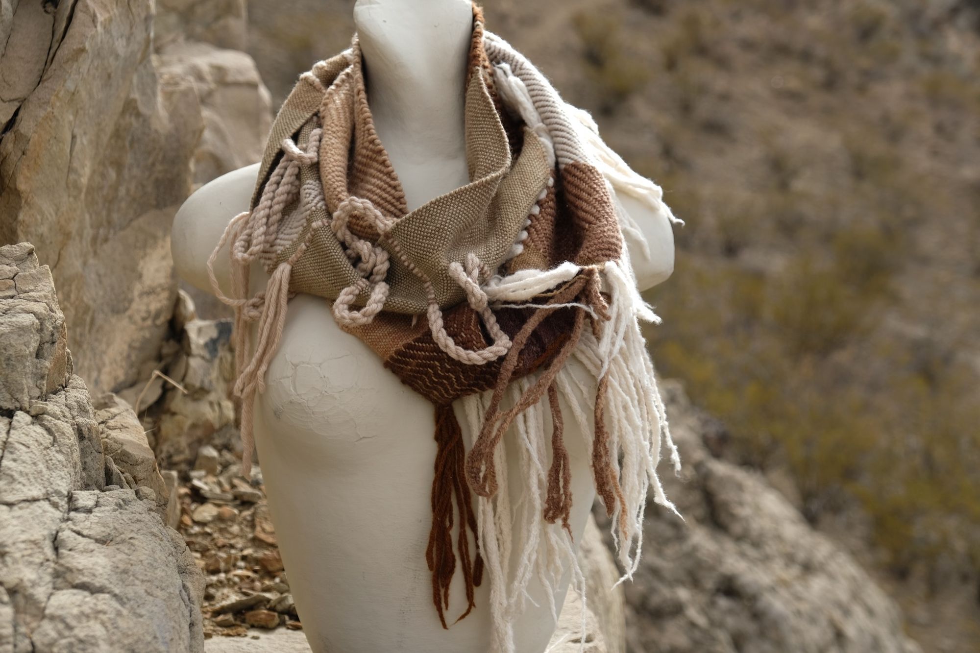 naturally dyed brown, tan, white and green highly fringed and textural infinity scarf on a white mannequin bust in the desert