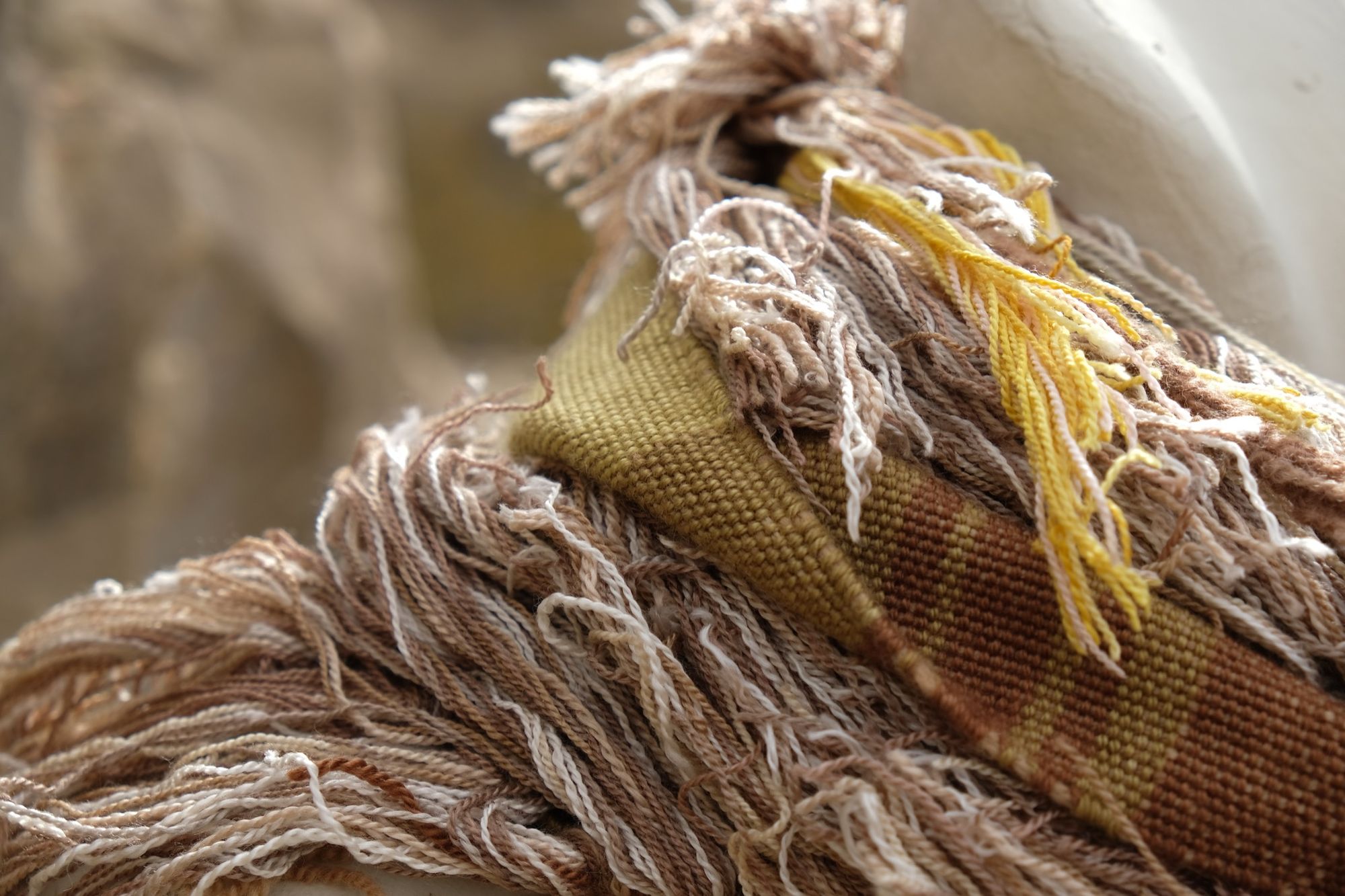 detail of naturally dyed brown, golden yellow and tan fringed infinity scarf on a white mannequin bust in the desert