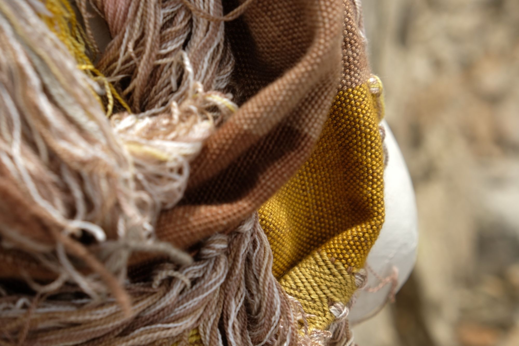 detail of naturally dyed brown, golden yellow and tan fringed infinity scarf on a white mannequin bust in the desert