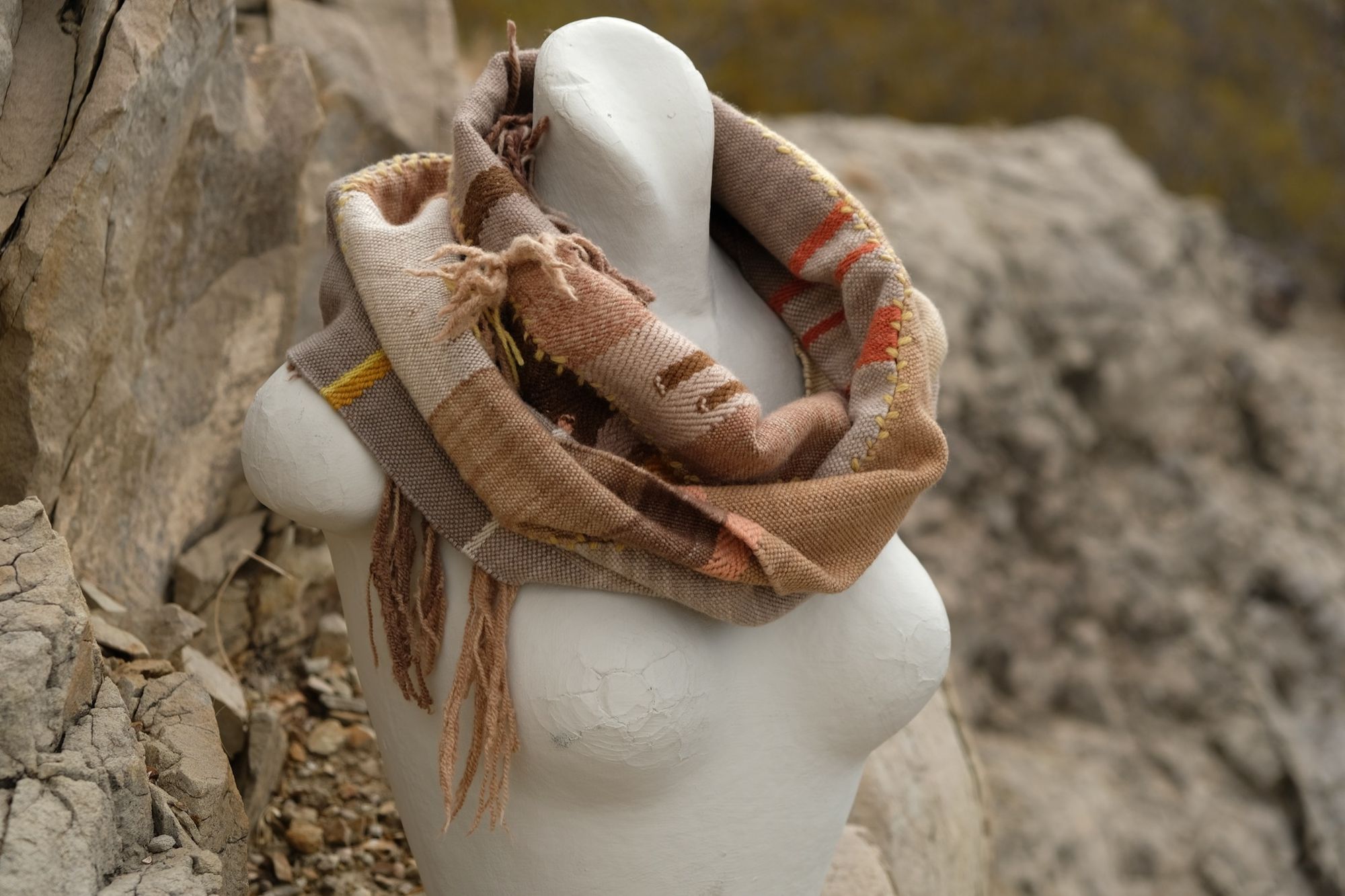 naturally dyed brown, yellow, pink, red and tan fringed infinity scarf on a white mannequin bust in the desert