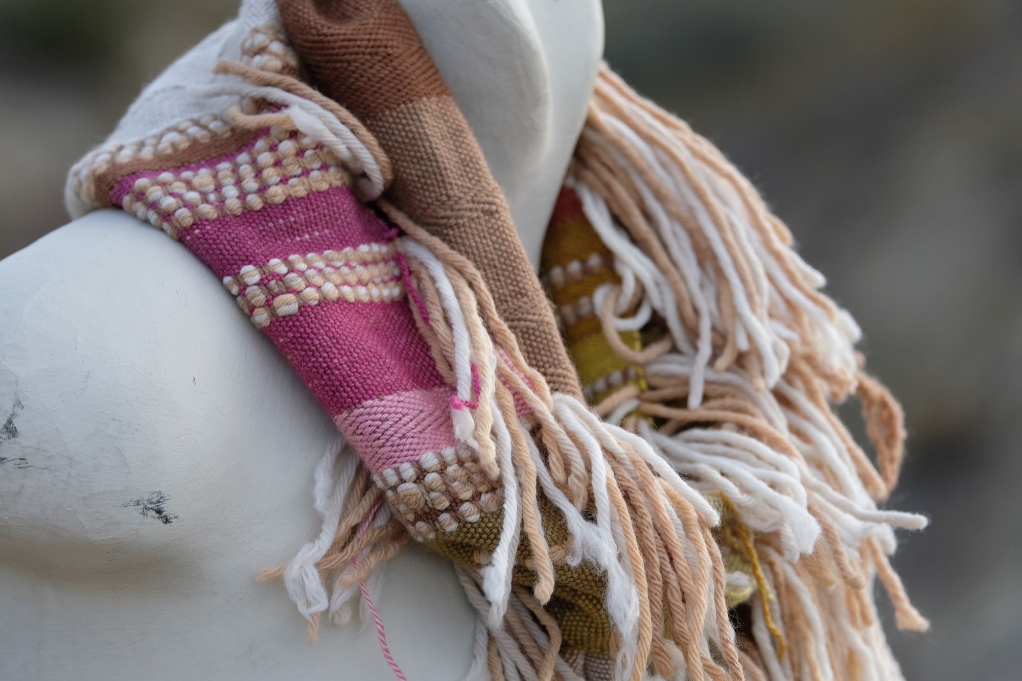 Detail of a naturally dyed brown, white, pink, salmon, yellow and green highly textured scarf on a white mannequin bust in the desert