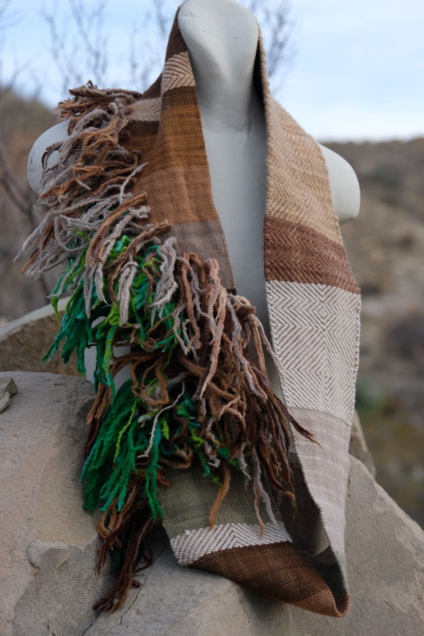 naturally dyed brown, tan white and green infinity scarf on a white mannequin bust in the desert