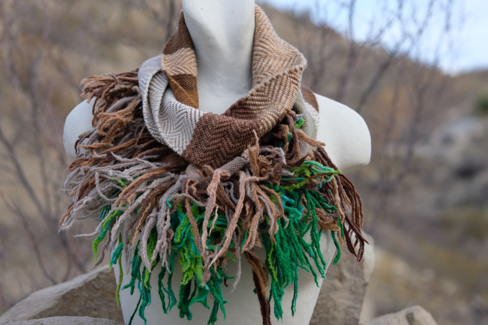 naturally dyed brown, tan white and green infinity scarf on a white mannequin bust in the desert