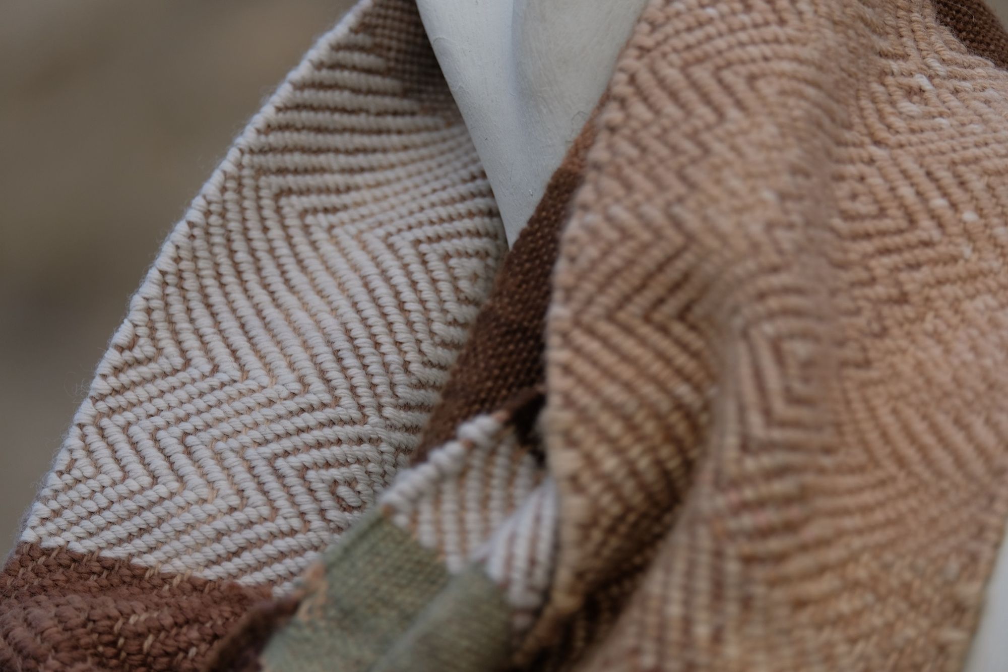detail of naturally dyed brown, tan white and green infinity scarf on a white mannequin bust in the desert