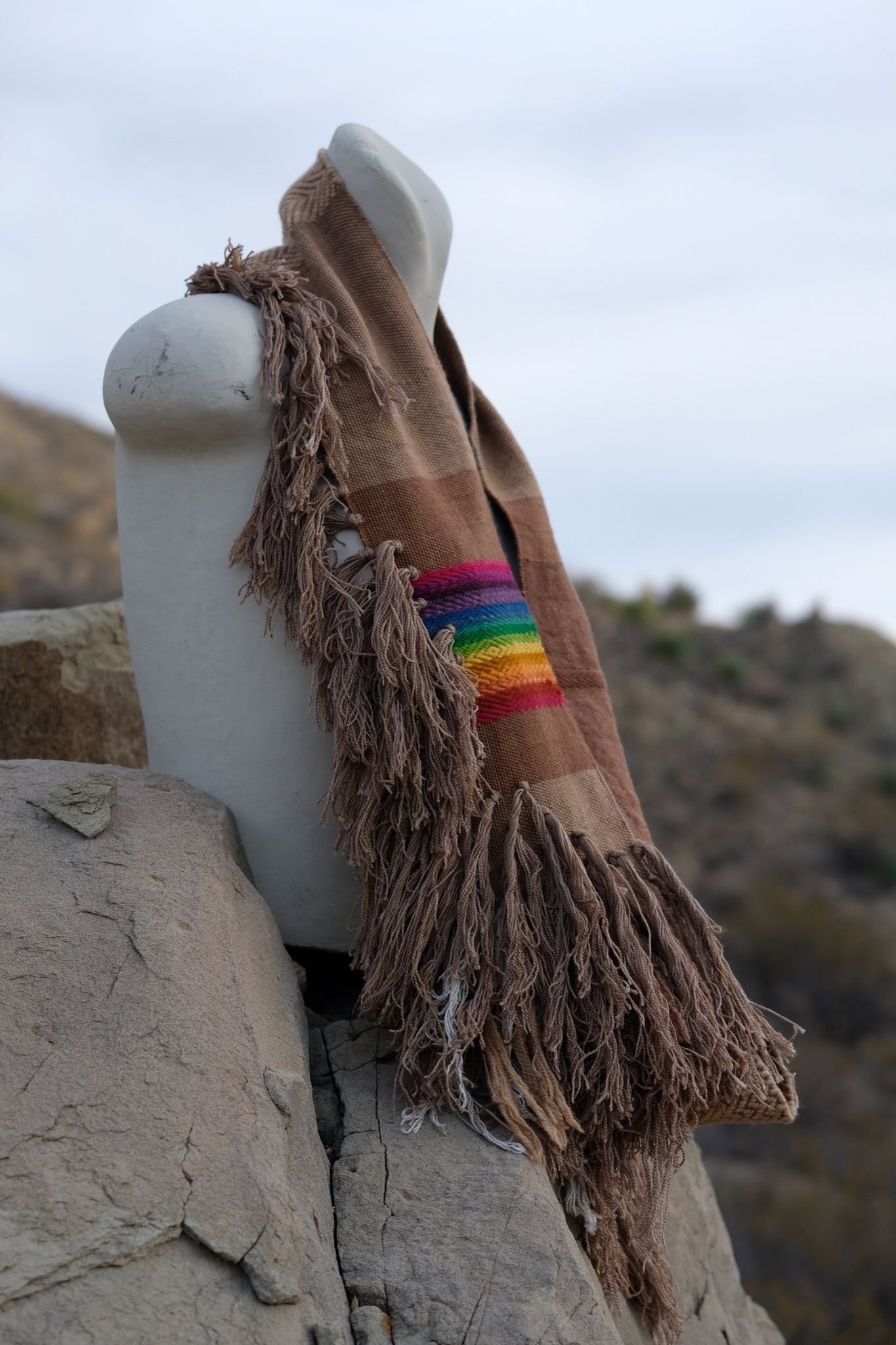 rainbow and naturally dyed brown fringed infinity scarf on a white mannequin bust in the desert