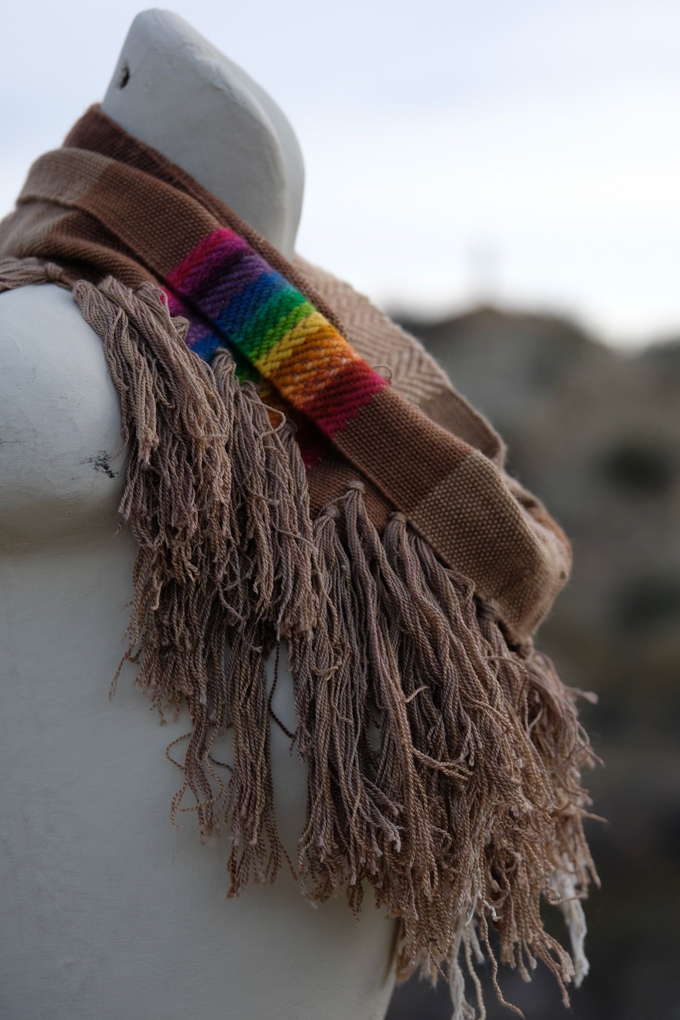 rainbow and naturally dyed brown fringed infinity scarf on a white mannequin bust in the desert