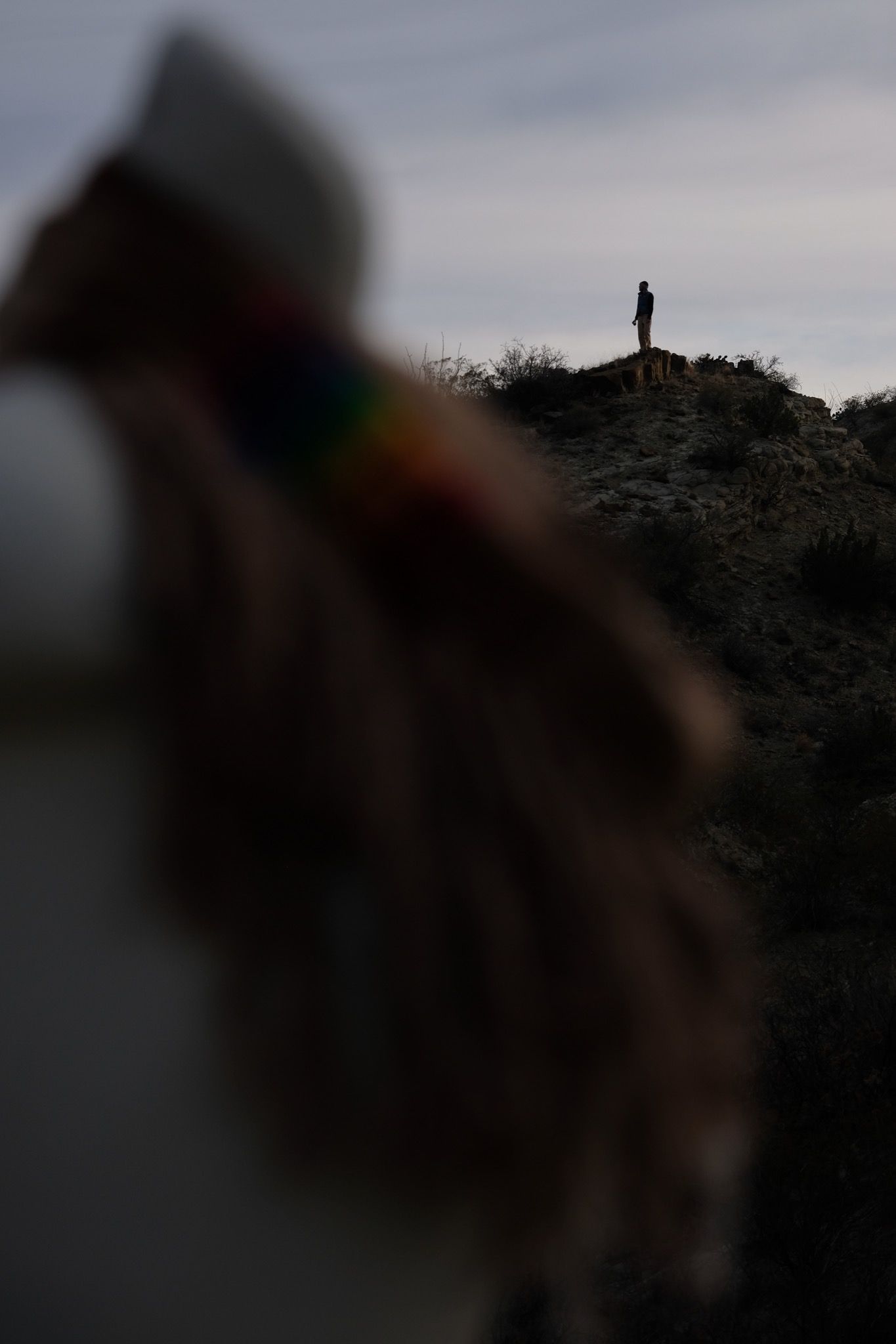 silhouette of a person in the background of rainbow and naturally dyed brown fringed infinity scarf on a white mannequin bust in the desert