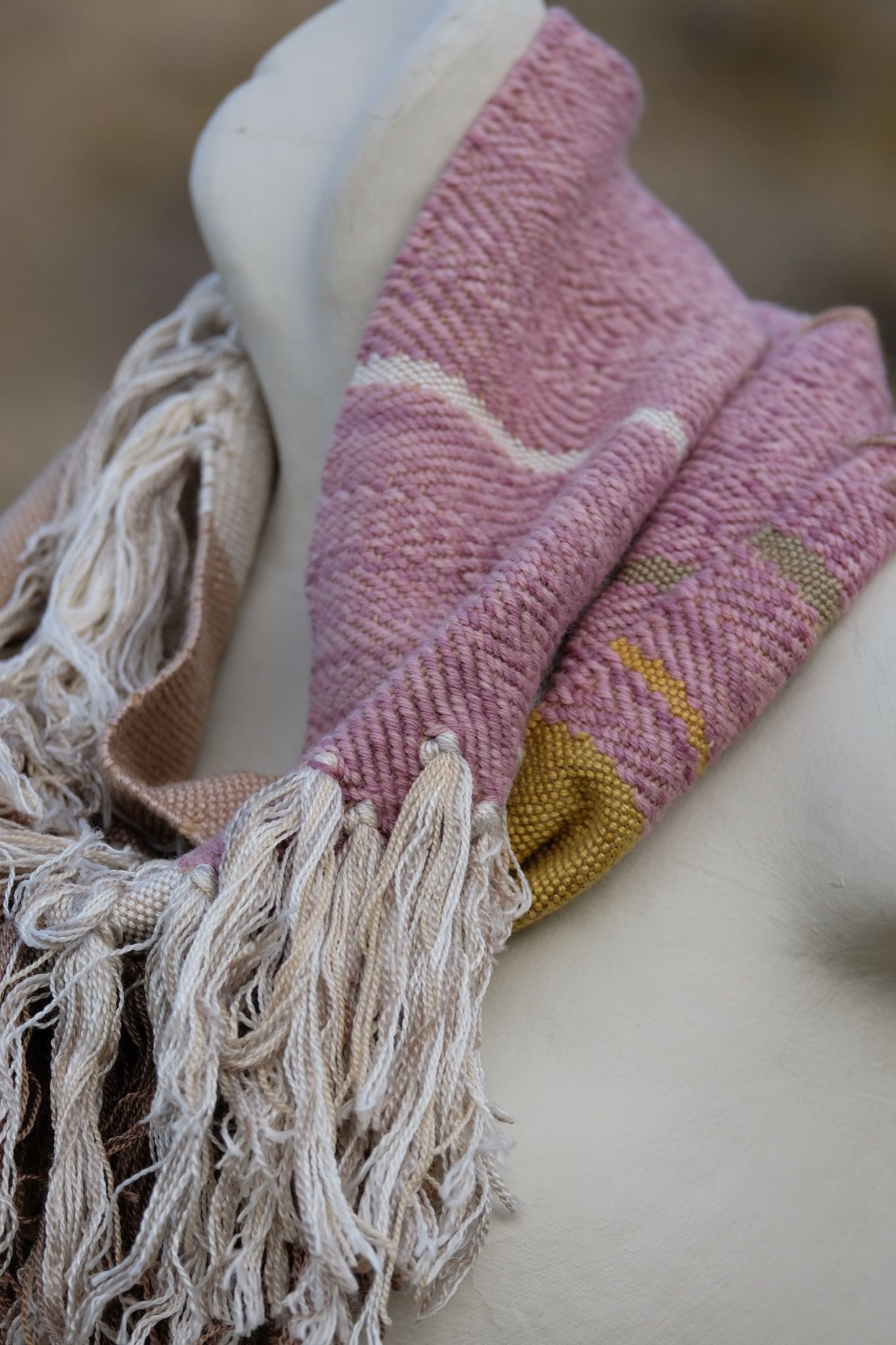 detail of naturally dyed brown, tan white, mauve and gold infinity scarf on a white mannequin bust in the desert