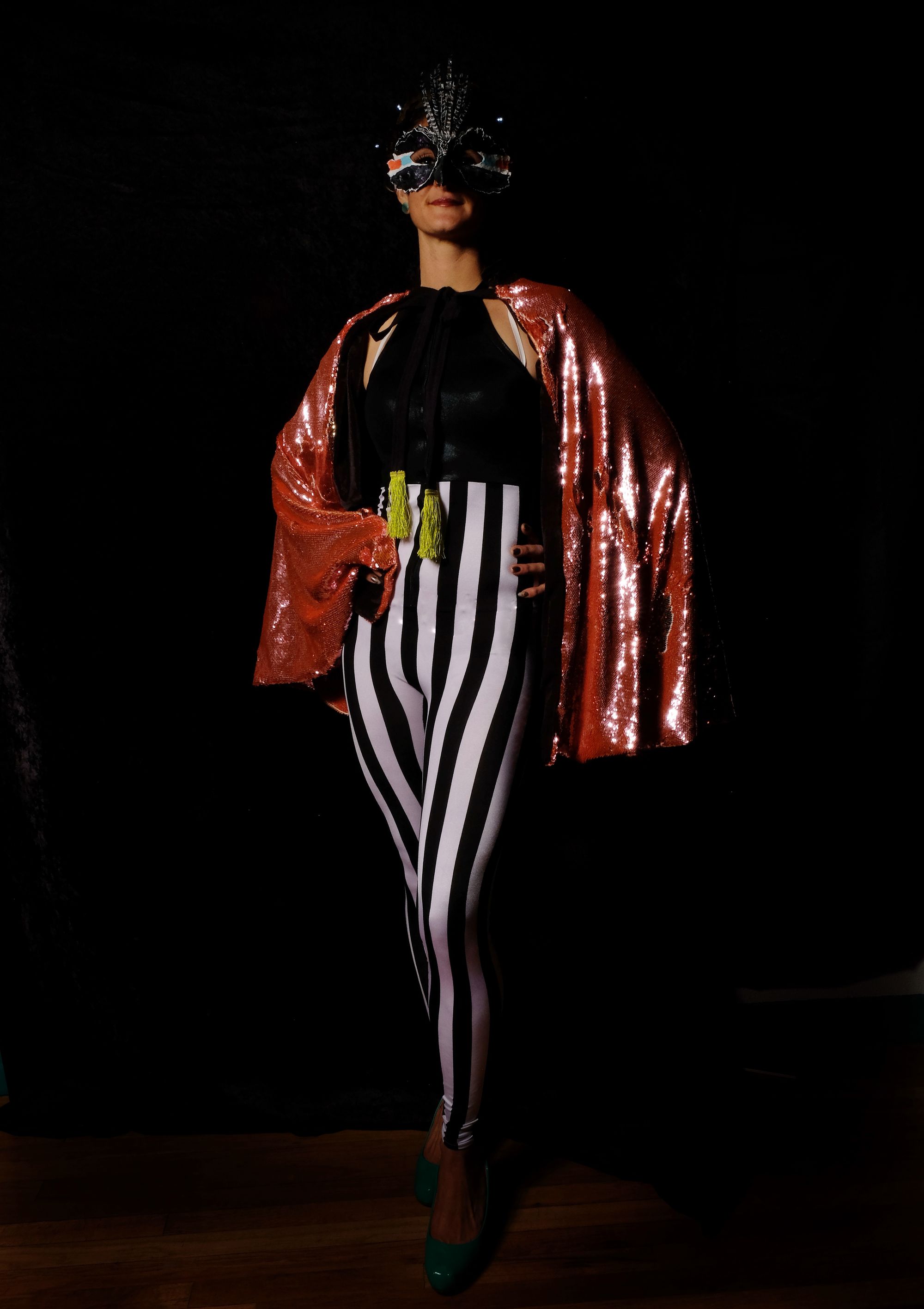 Woman in black and white striped costume with pink sequined cape and bird mask