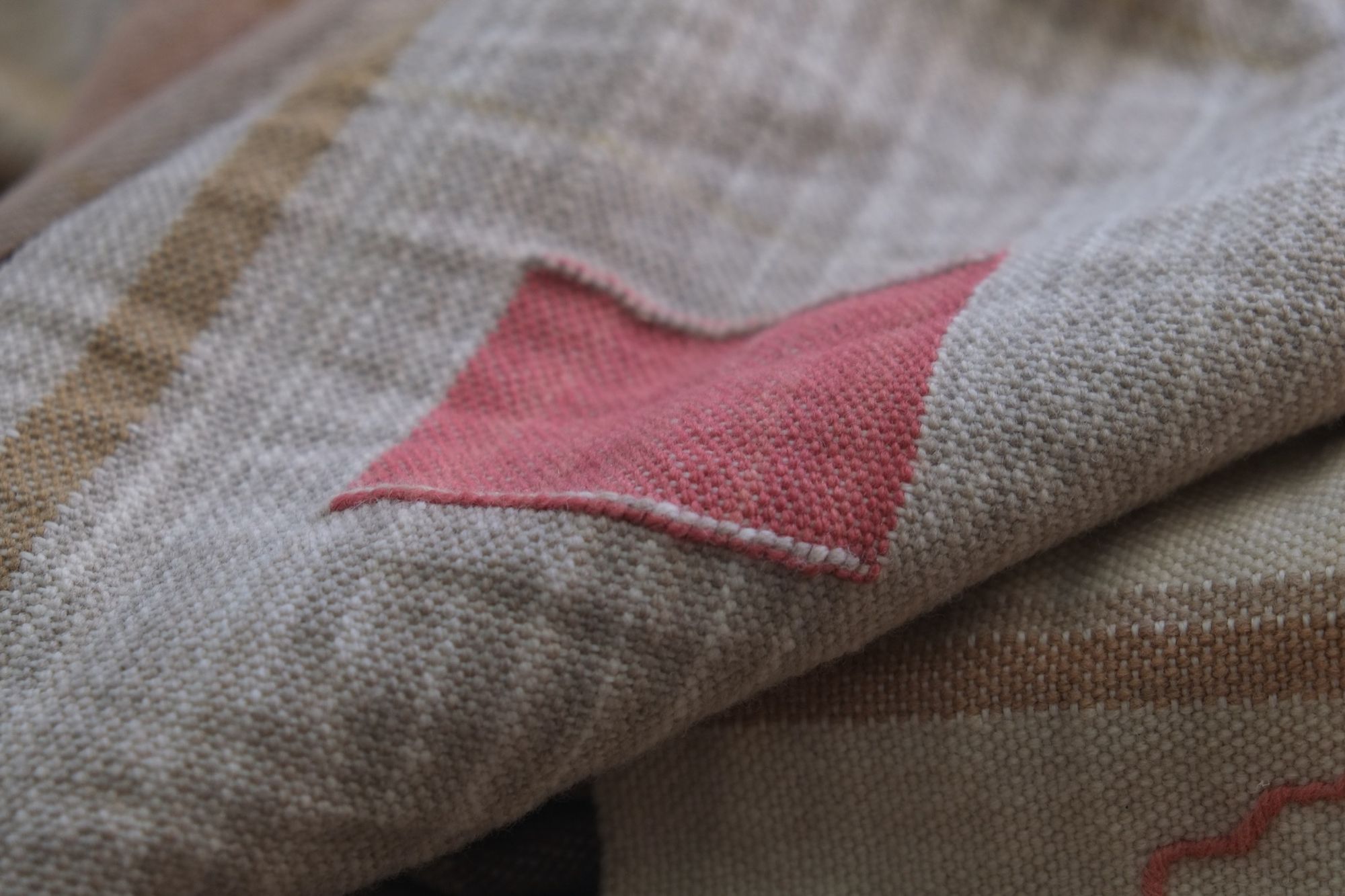 Detail of sandalwood color tapestry woven square, Handwoven Naturally Dyed Merino Ancient Dialogue Blanket laying on a wooden floor