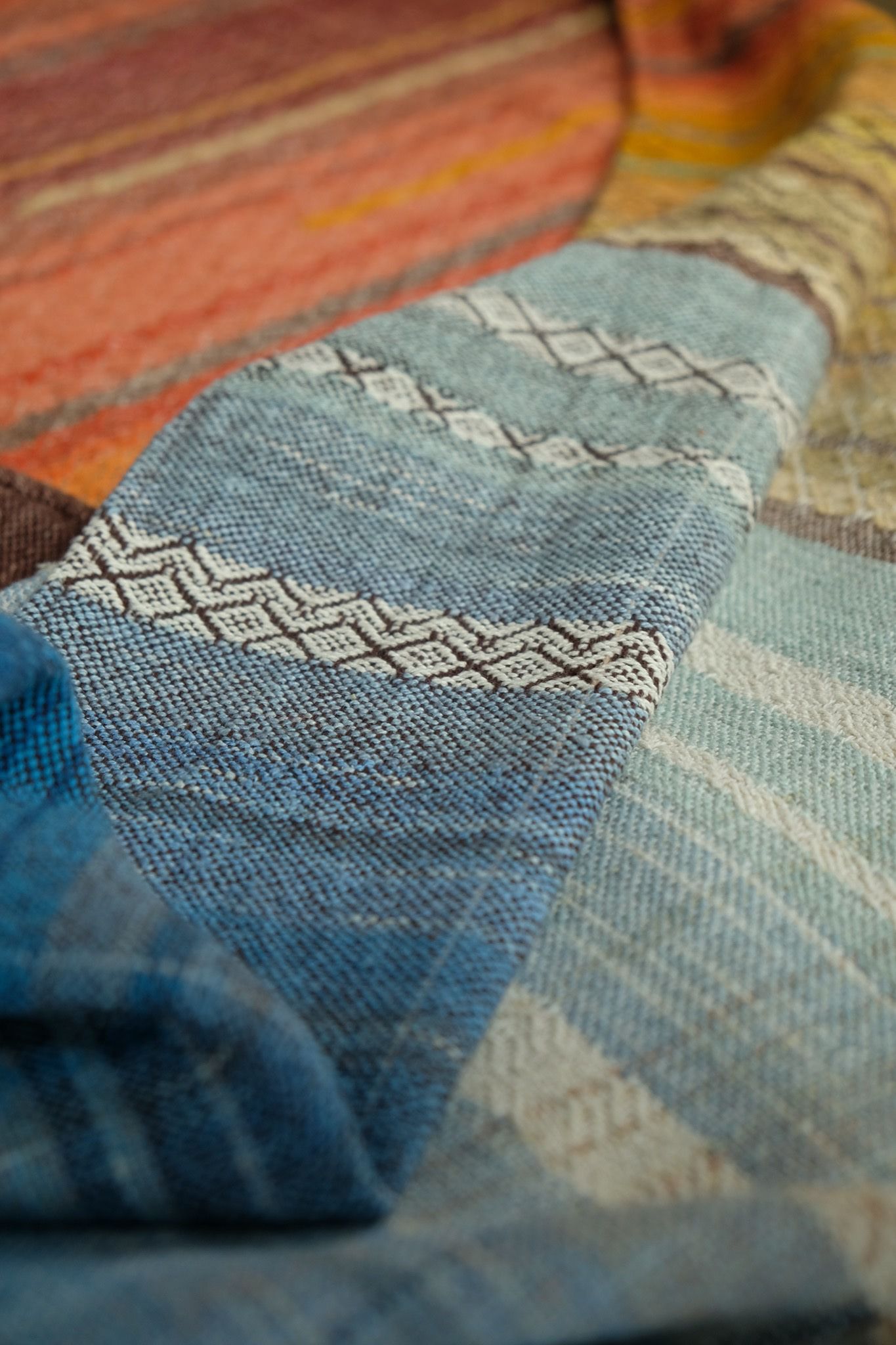detail of Large brown, red, orange, yellow, blue and green piece of handwoven fabric laying on a wooden floor. 