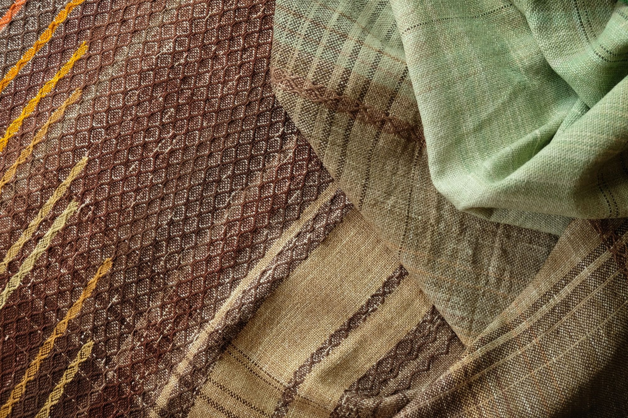 detail of Large brown, red, orange, yellow, blue and green piece of handwoven fabric laying on a wooden floor. 
