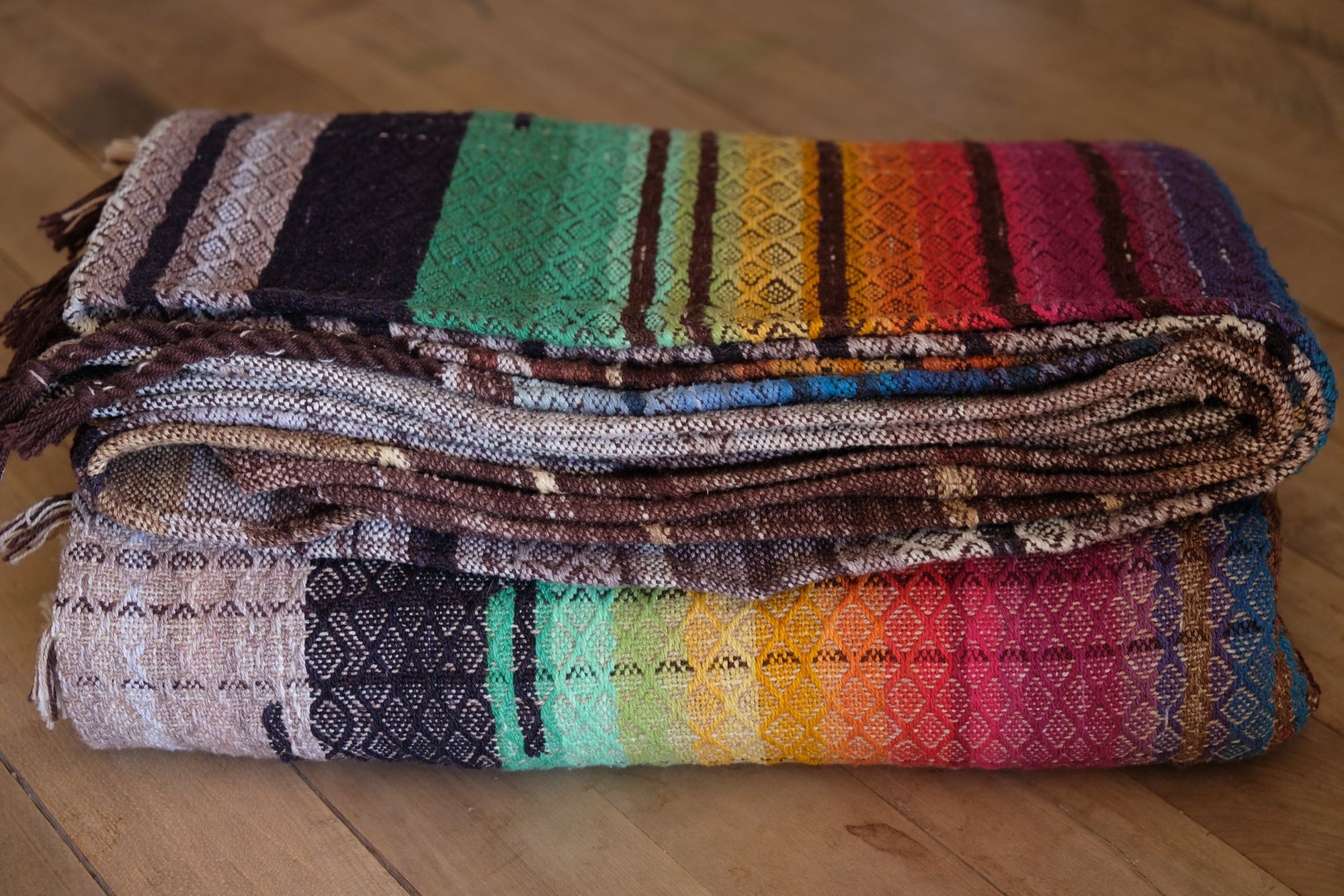 Multi colored handwoven raw silk fabric, folded and laying on a wooden floor