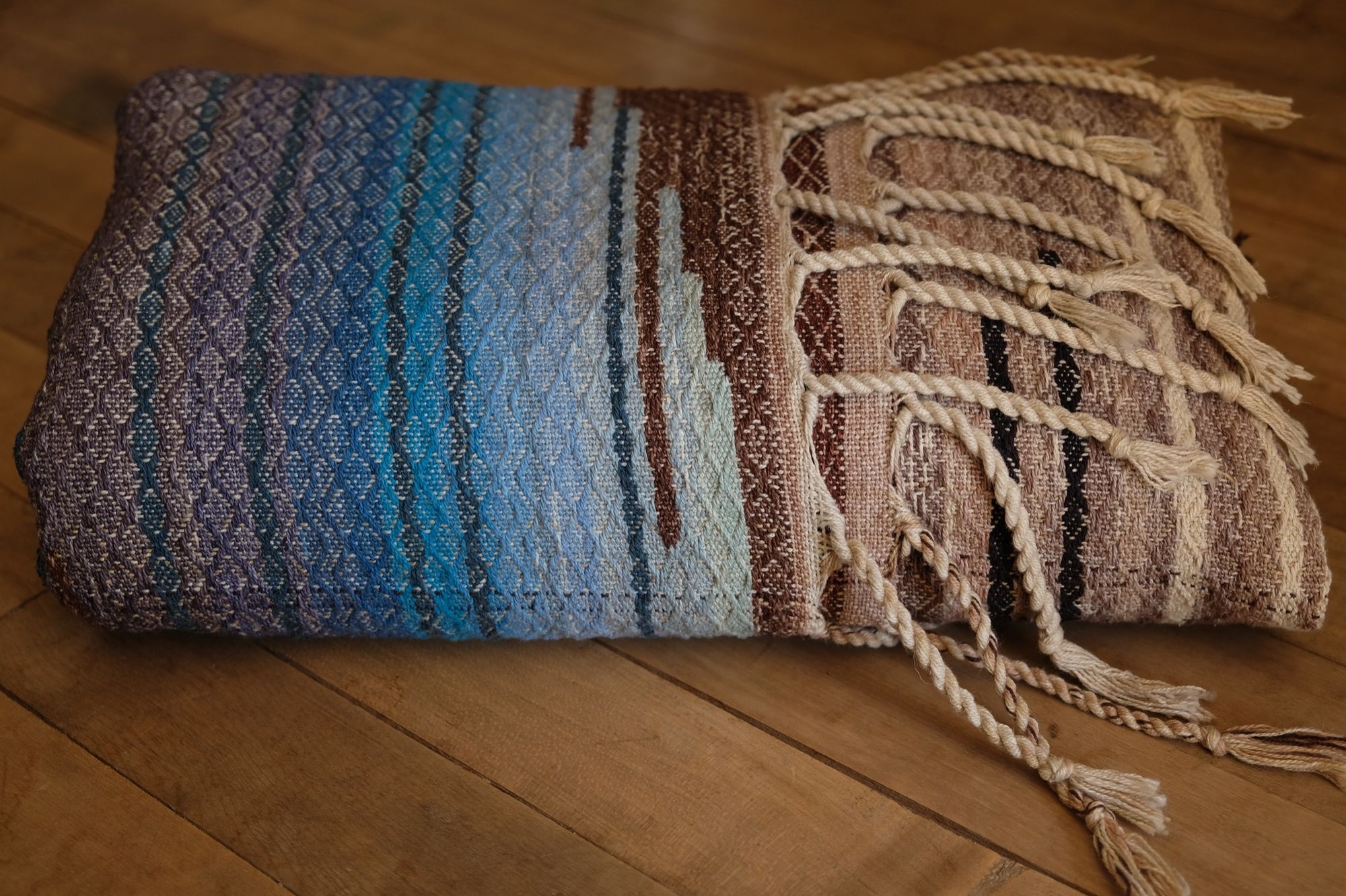 Multi colored handwoven raw silk fabric, folded and laying on a wooden floor
