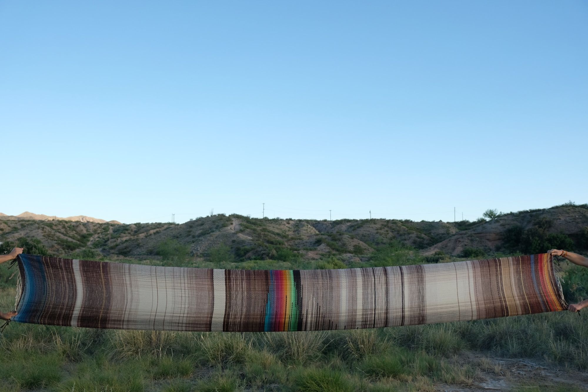 Multi colored handwoven raw silk fabric being held up by two people in the desert
