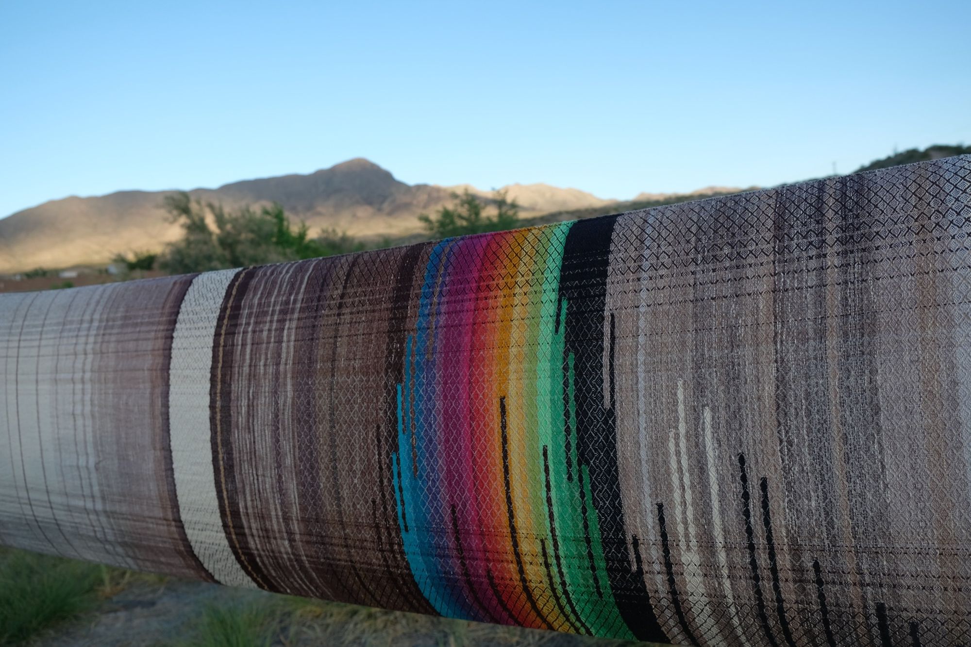 detail of Multi colored handwoven raw silk fabric being held up by two people in the desert