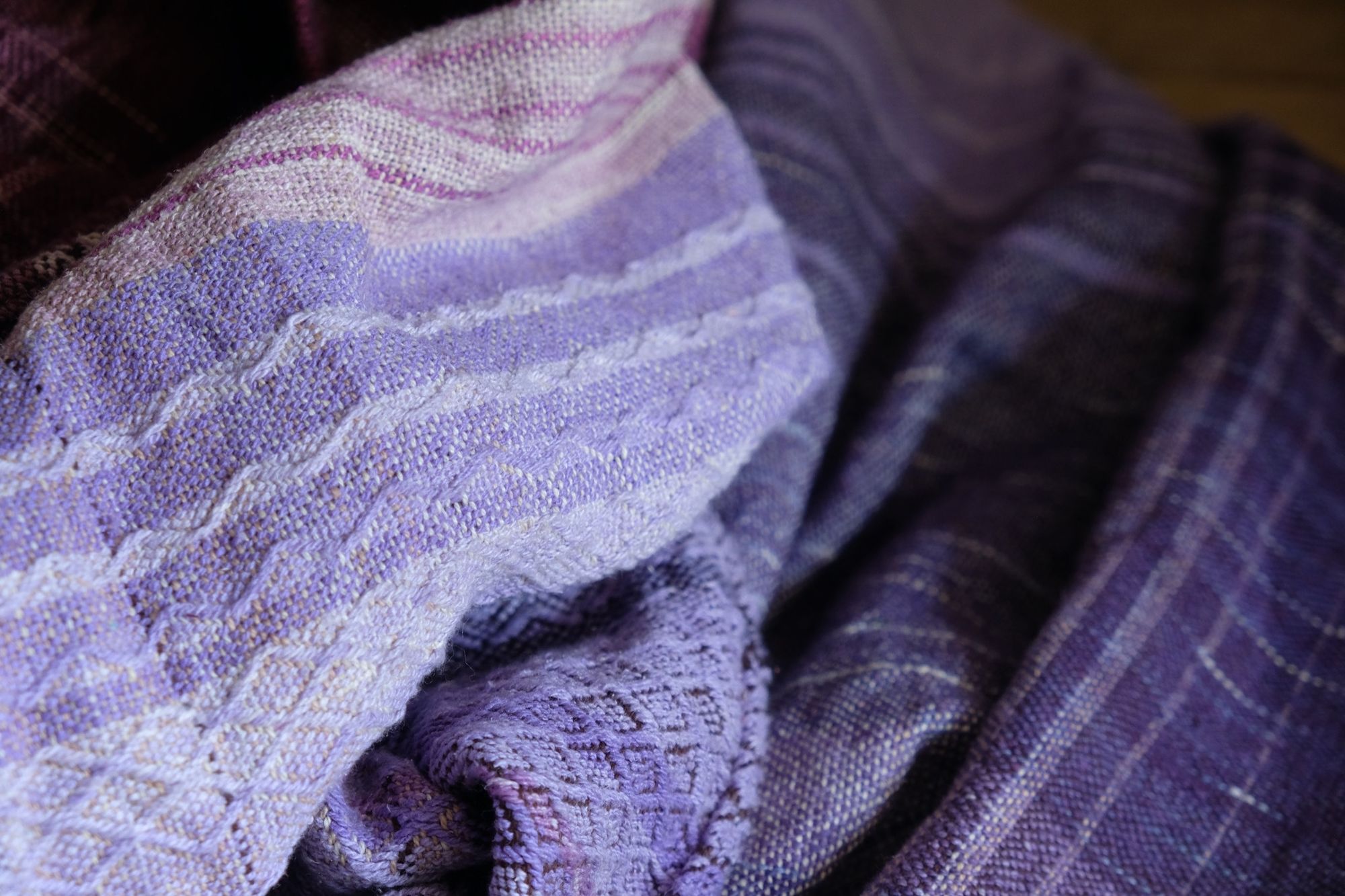 Brightly colored purple, blue, orange, green, black and pink handwoven fabric laying on a wooden floor. 