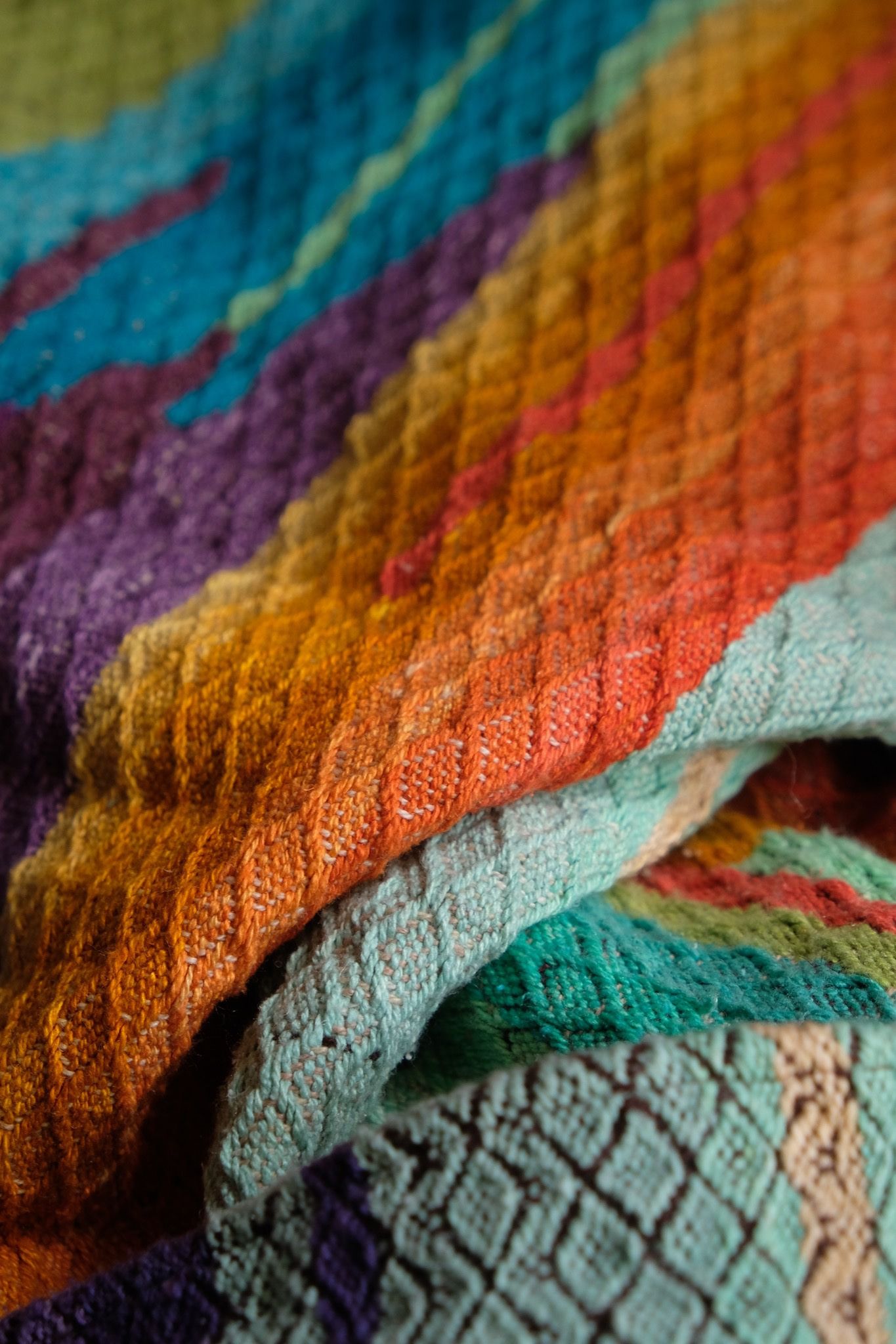 Brightly colored purple, blue, orange, green, black and pink handwoven fabric laying on a wooden floor. 