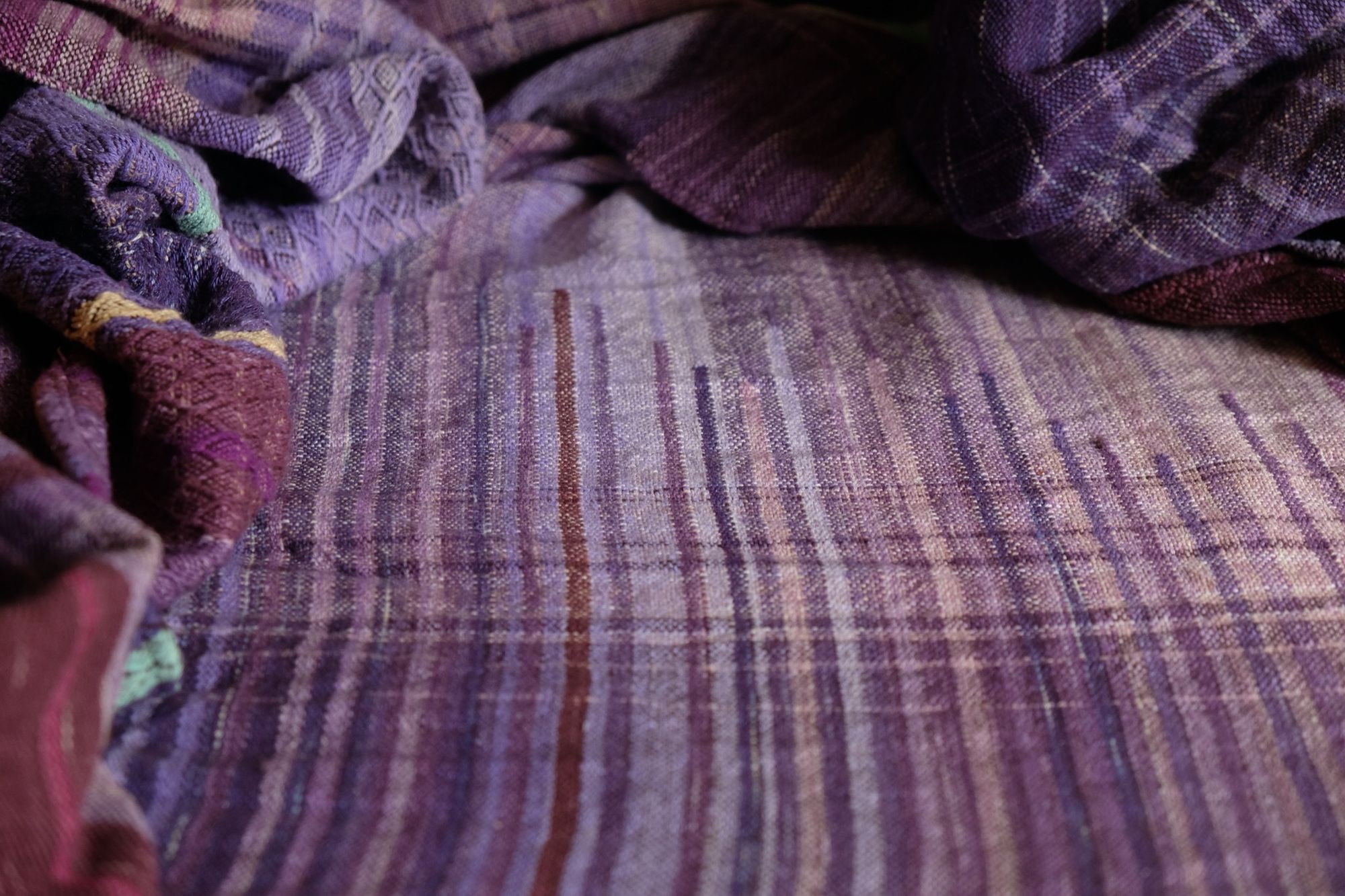 Brightly colored purple, blue, orange, green, black and pink handwoven fabric laying on a wooden floor. 