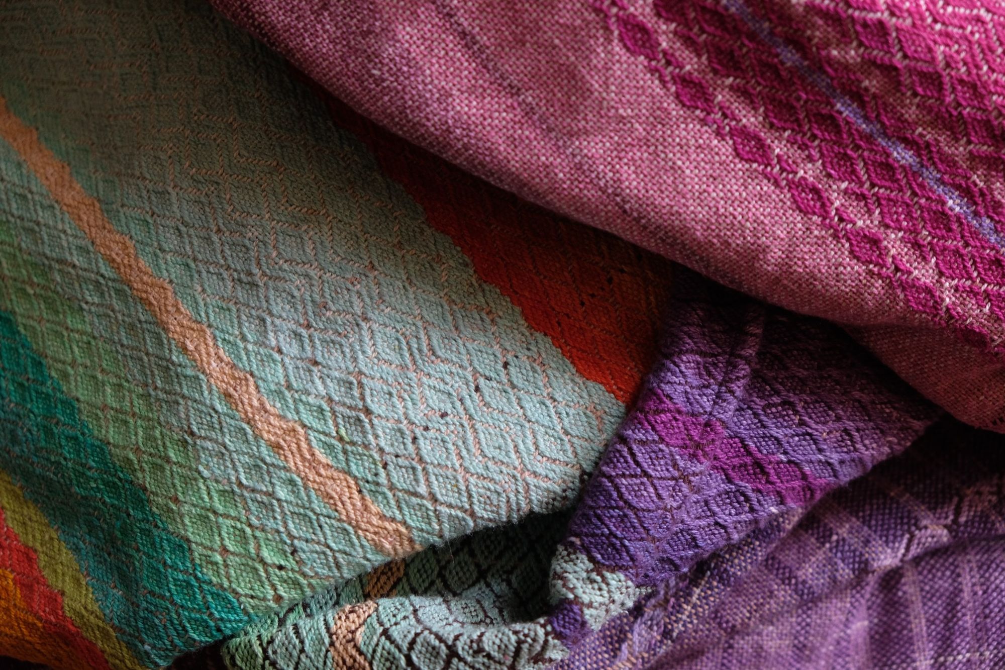 Brightly colored purple, blue, orange, green, black and pink handwoven fabric laying on a wooden floor. 