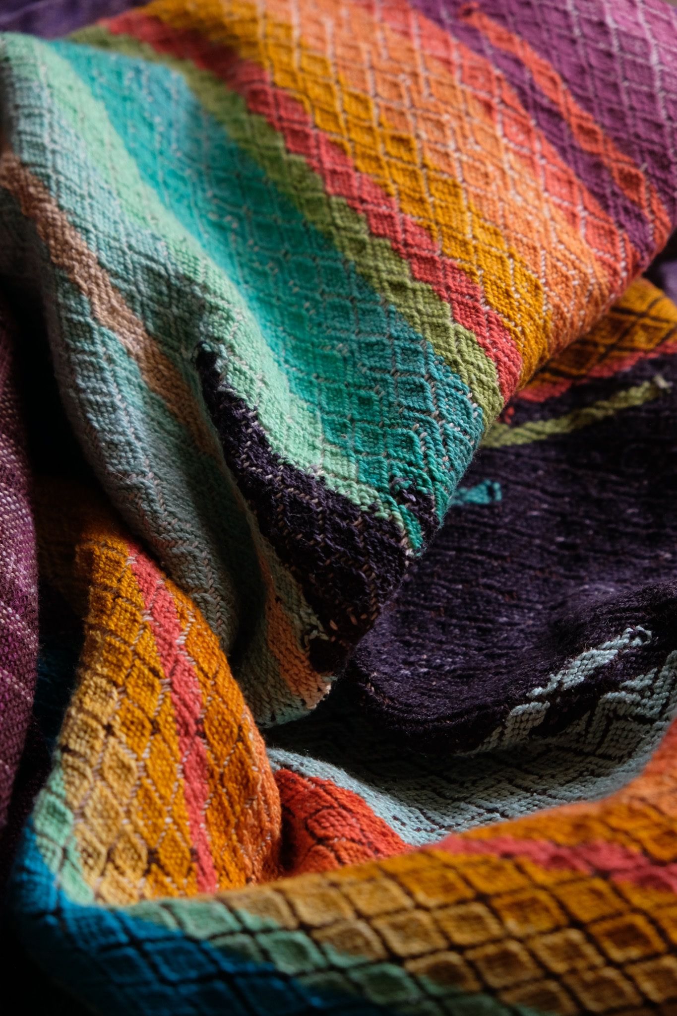 Brightly colored purple, blue, orange, green, black and pink handwoven fabric laying on a wooden floor. 