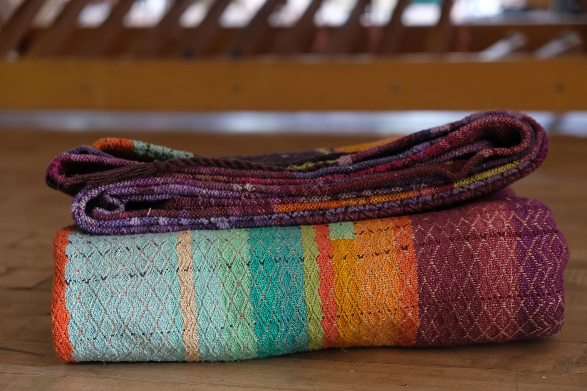 Brightly colored purple, blue, orange, green, black and pink handwoven fabric laying on a wooden floor. 