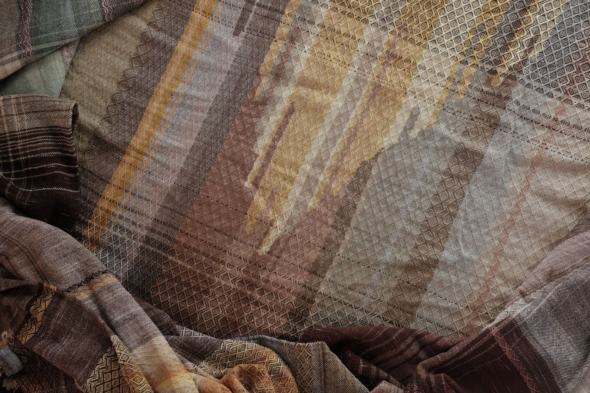 detail of soft yellow, green, orange and brown Handwoven fabric laying on a wood floor