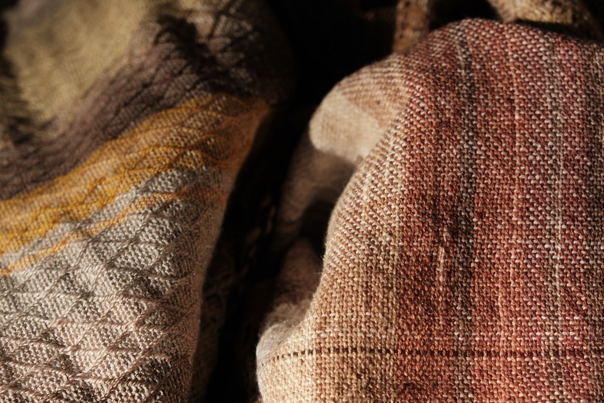 detail of soft yellow, green, orange and brown Handwoven fabric laying on a wood floor
