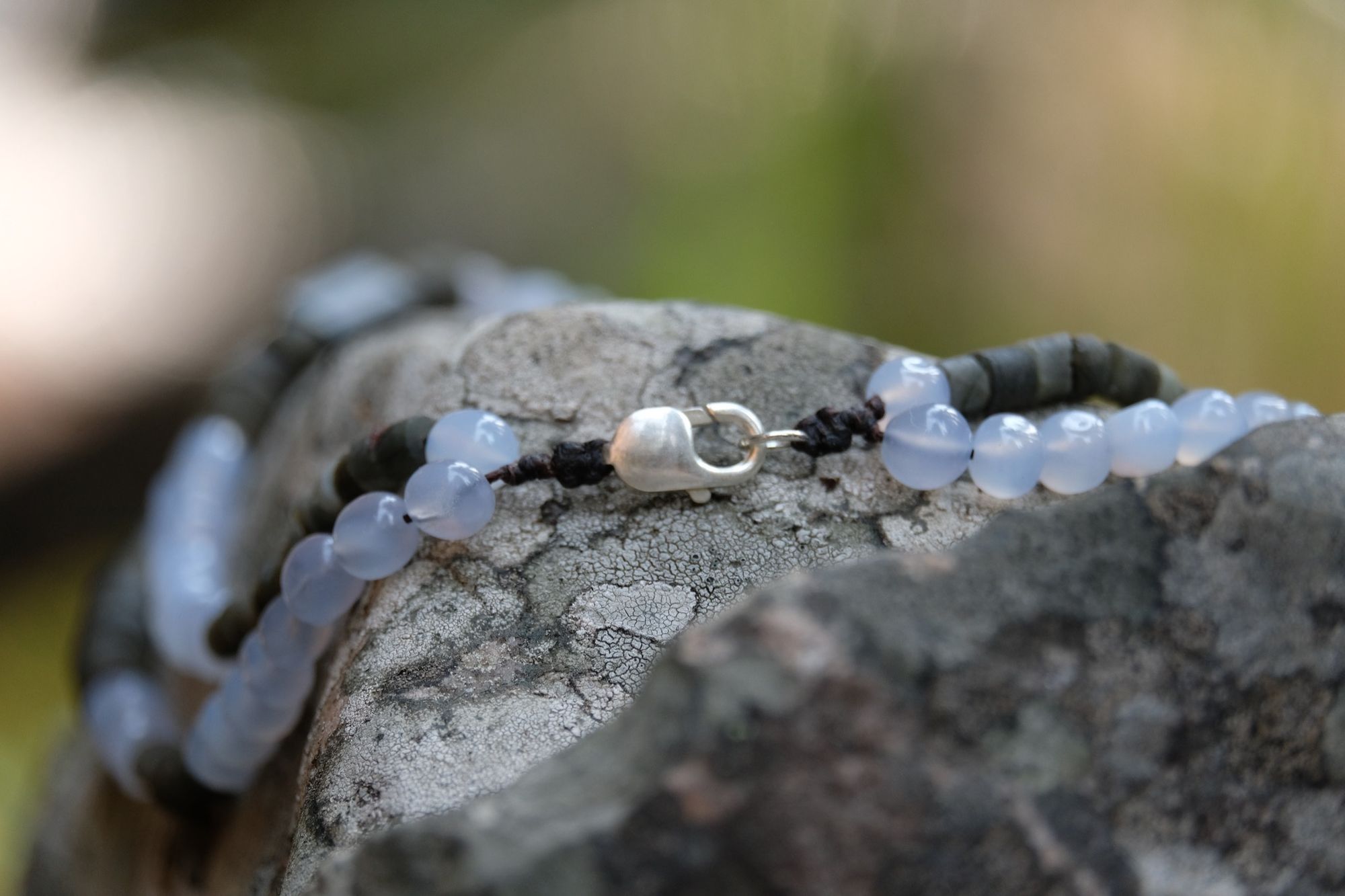 detail of two strand necklace with Smoky quartz, quartz, luminous blue carnelian, labradorite and black tourmaline sitting on a boulder